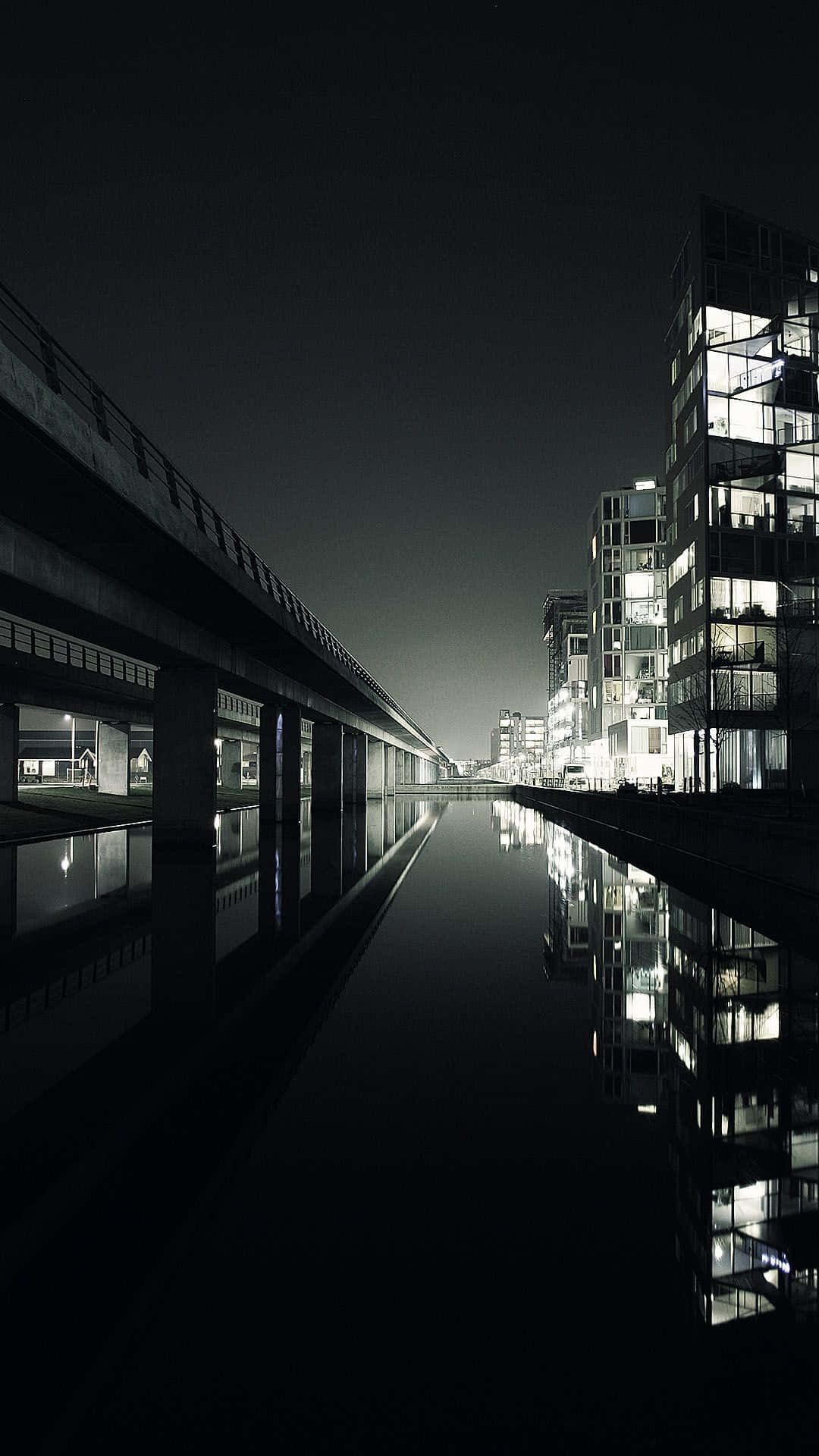 Modern Aesthetic 桌布 壁紙 — 一條運河的單色夜景，兩旁是現代玻璃建築和高架橋，發光的窗戶倒映在平靜的水面上。