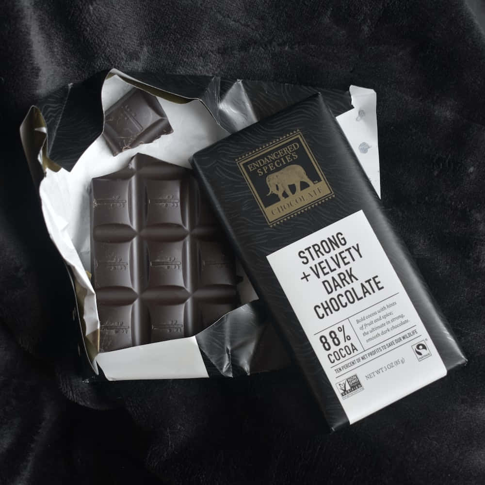 Dark Chocolate 桌布 壁紙 — 一條部分包裝的88%黑巧克力棒放在柔軟的黑色布料上，展現其豐富的質感和大膽的標籤。