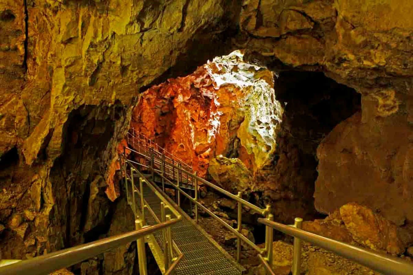 Cave 桌布 壁紙 — 一條金屬步道蜿蜒穿過洞穴，洞穴內有發光的橙色和白色礦物形成物，襯托著粗糙的棕色岩壁。