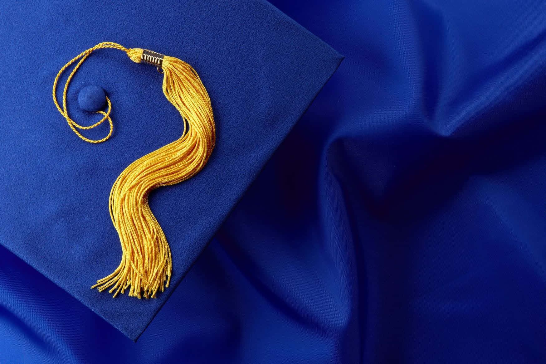 Graduation 桌布 壁紙 — 一條金色流蘇優雅地放在皇家藍色畢業帽上，背景是相配的布料。