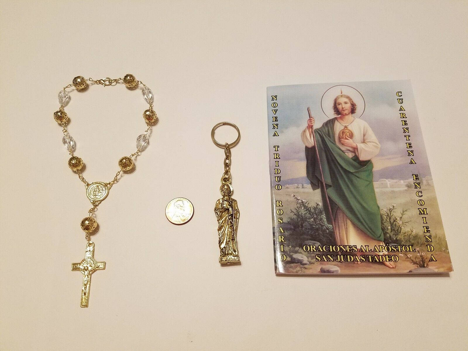religion 桌布 壁紙 — 一條金色透明珠子玫瑰經念珠、一個聖人鑰匙圈和一本聖猶達祈禱手冊，放在純米白色表面上。
