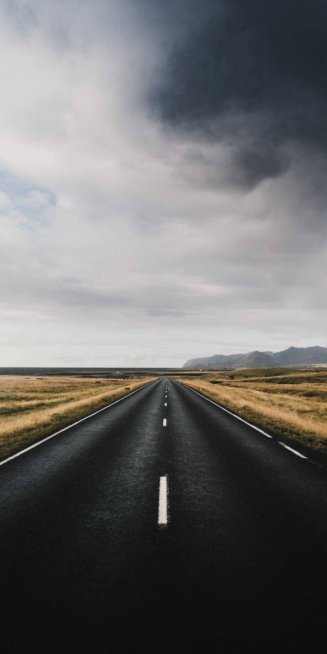 Country Road 桌布 壁紙 — 一條長直瀝青道路在戲劇性的多雲天空下延伸向遠山。