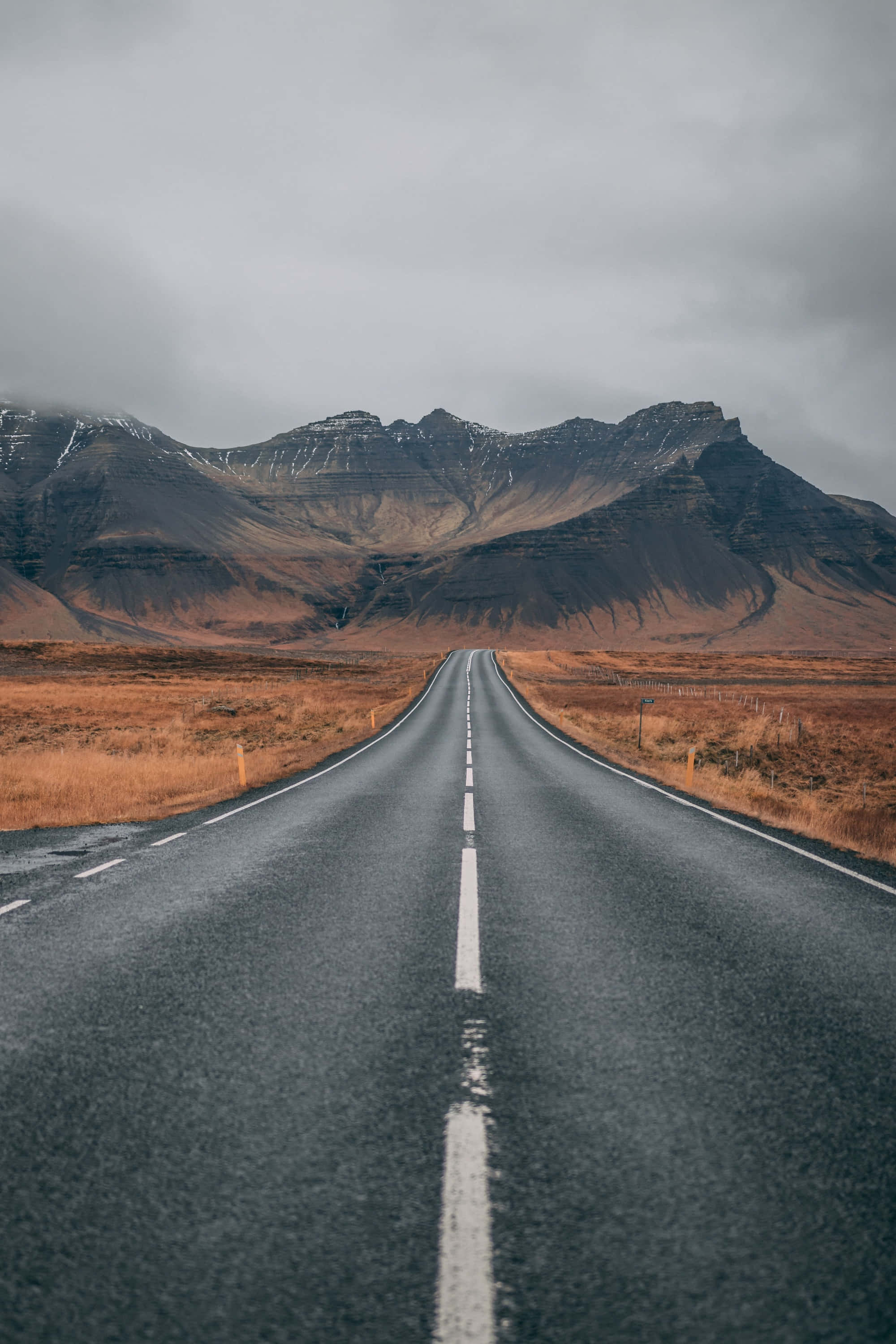 highway 桌布 壁紙 — 一條長直路延伸至遠山，天空多雲，兩旁有乾草。