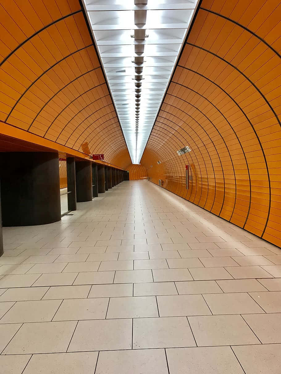 Subway 桌布 壁紙 — 一條長直隧道，帶有彎曲的橙色瓷磚牆壁和明亮的白色天花板燈光，向遠方延伸。