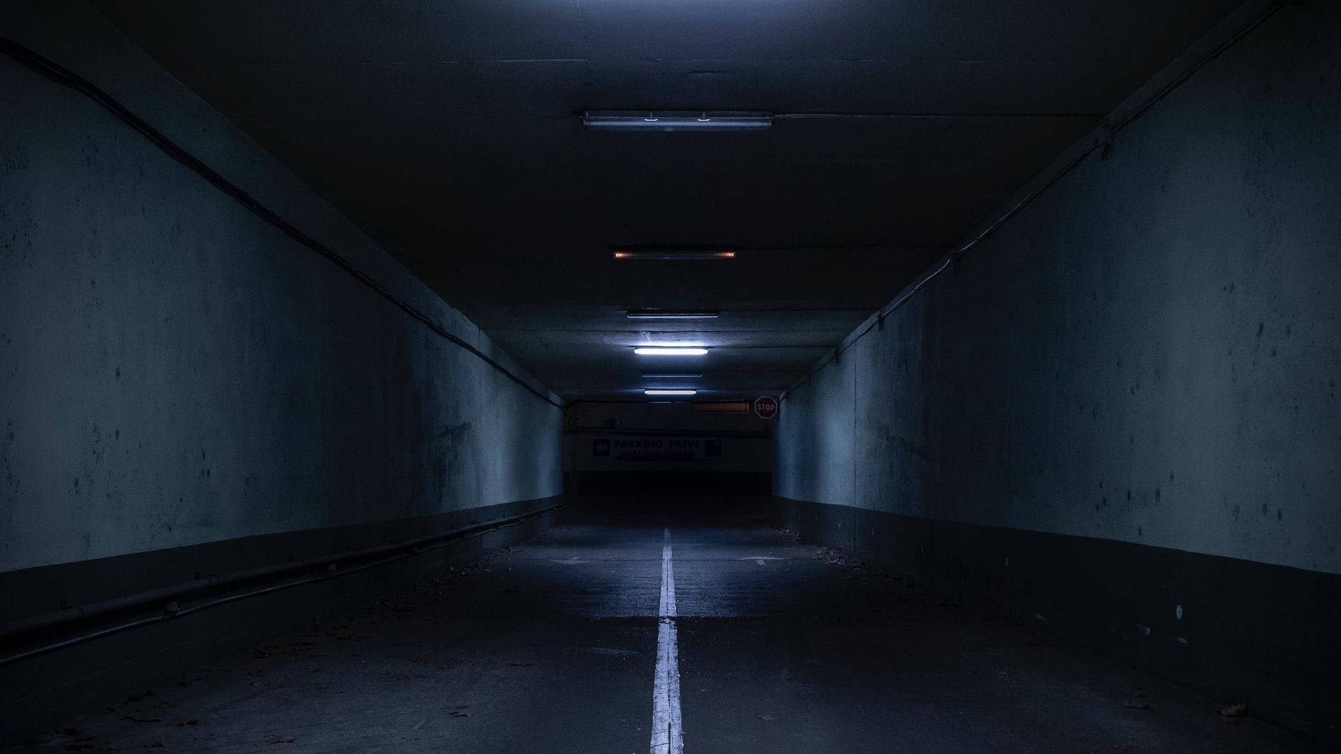 tunnel 桌布 壁紙 — 一條長而昏暗的地下停車場隧道，中央有一條白線，頭頂上有閃爍的螢光燈。