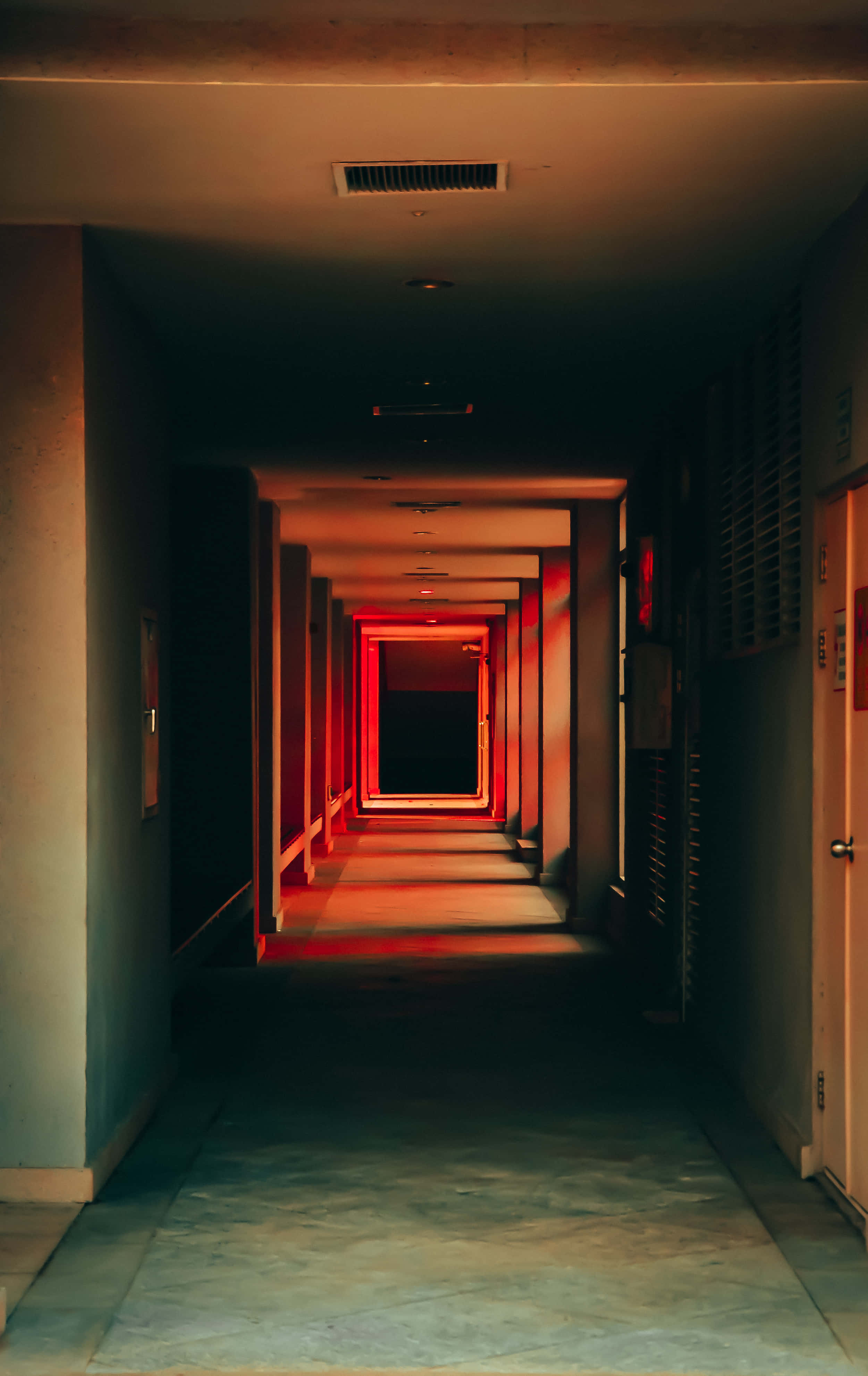 hallway 桌布 壁紙 — 一條長而昏暗的走廊，帶有溫暖的紅色燈光，逐漸消失在盡頭的黑暗中。