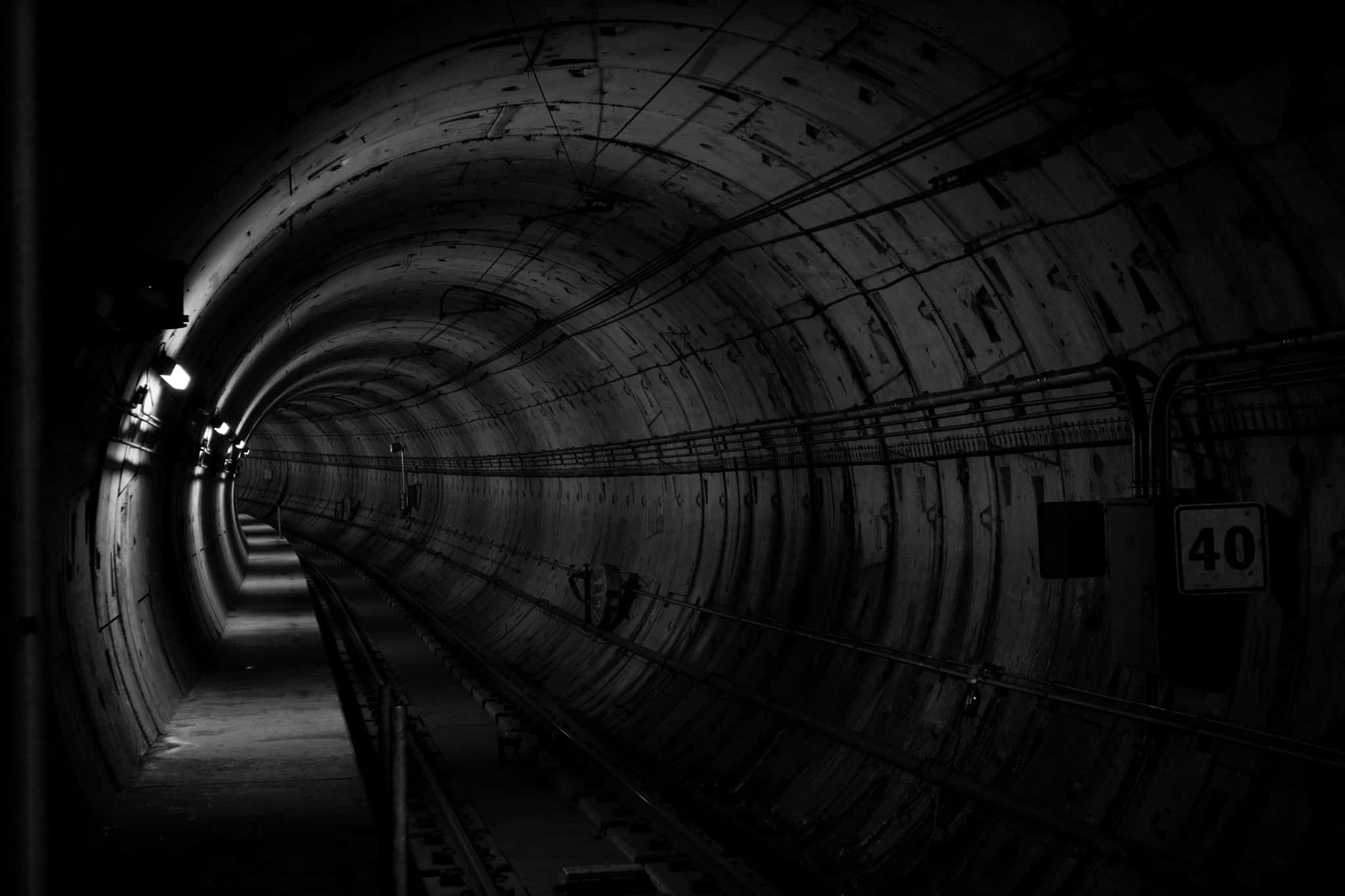Dark Underground 桌布 壁紙 — 一條長而黑暗的隧道，帶有彎曲的混凝土牆壁和鐵路軌道，逐漸消失在陰影深處。