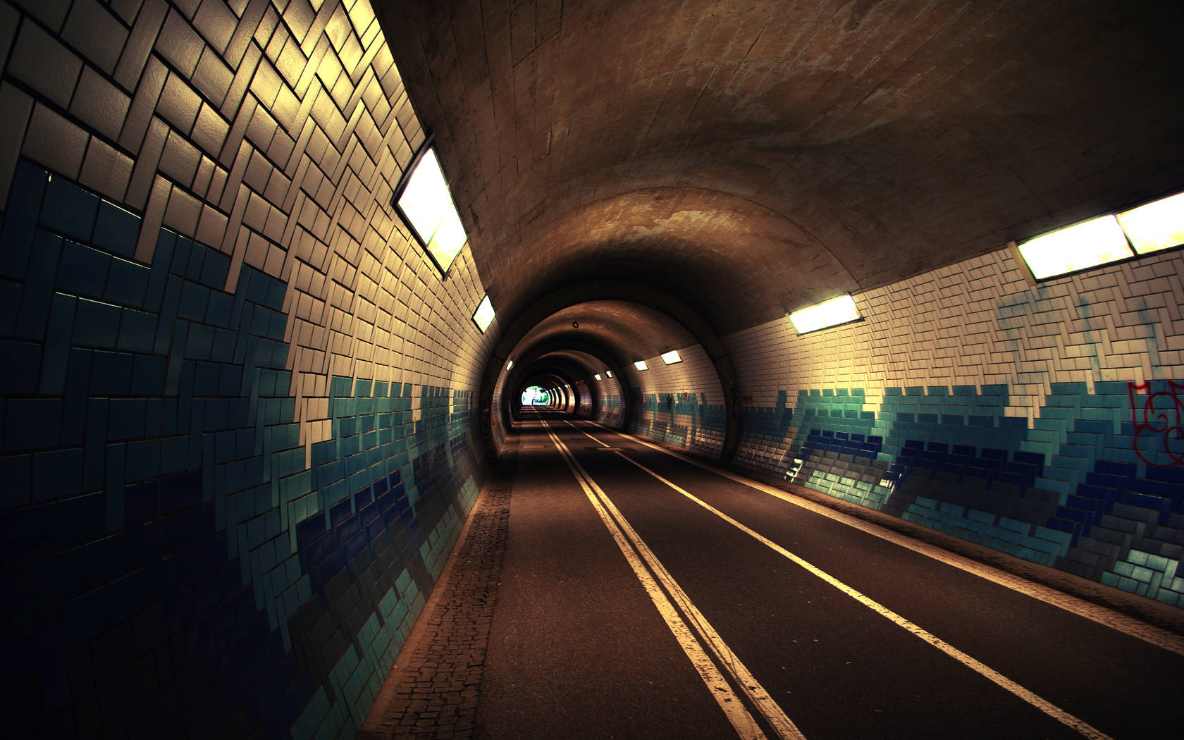 train tunnel 桌布 壁紙 — 一條長長、燈光昏暗的地鐵隧道，藍色瓷磚牆壁和發光的天花板燈光向遠方延伸。