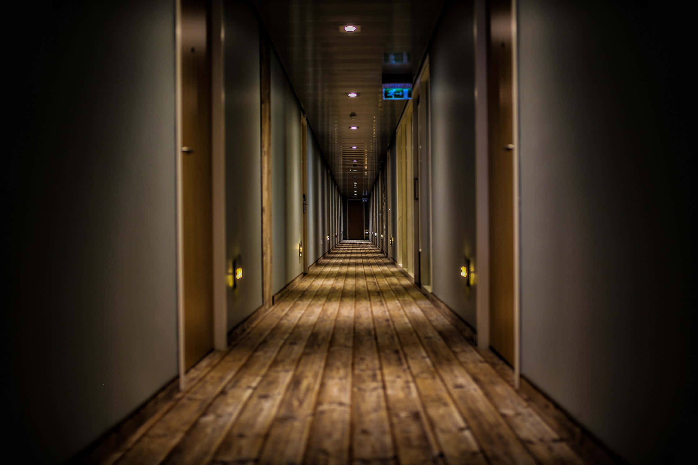 hallway 桌布 壁紙 — 一條長長的、燈光昏暗的飯店走廊，木地板和門在天花板燈光下逐漸消失在黑暗中。