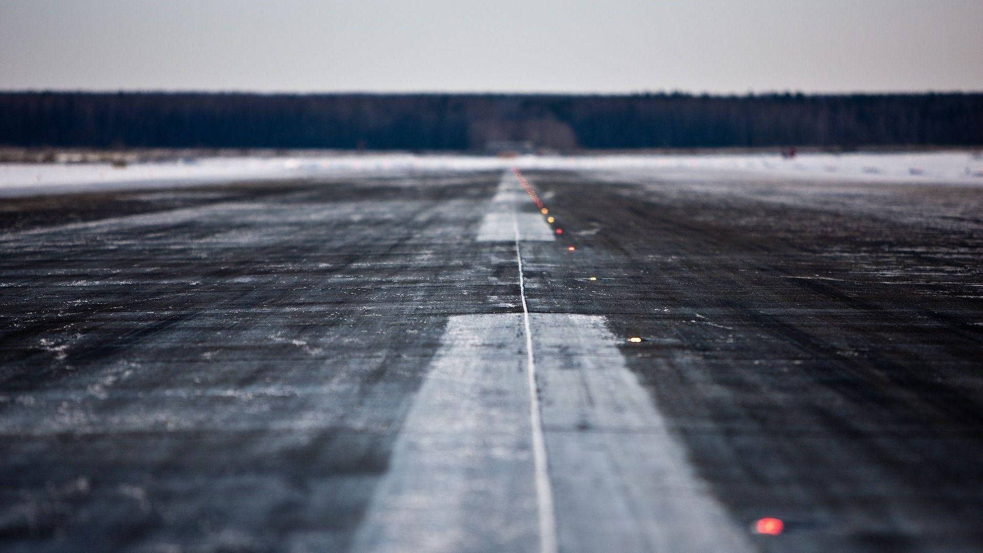 Runway 桌布 壁紙 — 一條長長的冰封跑道在蒼白的冬日天空下延伸至遠方，地平線上有積雪的樹木。