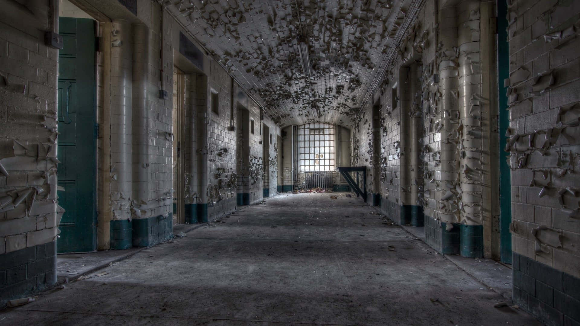 Prison Cell 桌布 壁紙 — 一條長長的廢棄監獄走廊，牆壁剝落、油漆脫落，盡頭有一扇鐵窗。