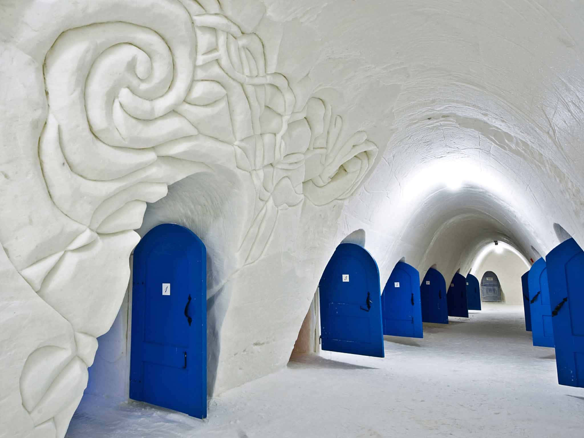 Ice Hotel 桌布 壁紙 — 一條長長的拱形走廊，帶有紋理白色牆壁和鮮豔的藍色門，逐漸消失在遠方。
