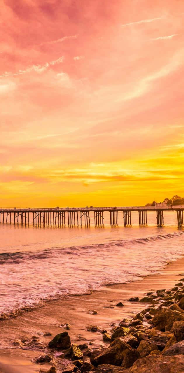 Beach Sunset HD 桌布 壁紙 — 一條長長的木碼頭延伸到平靜的水面上，天空呈現充滿活力的粉紅色和橙色日落。