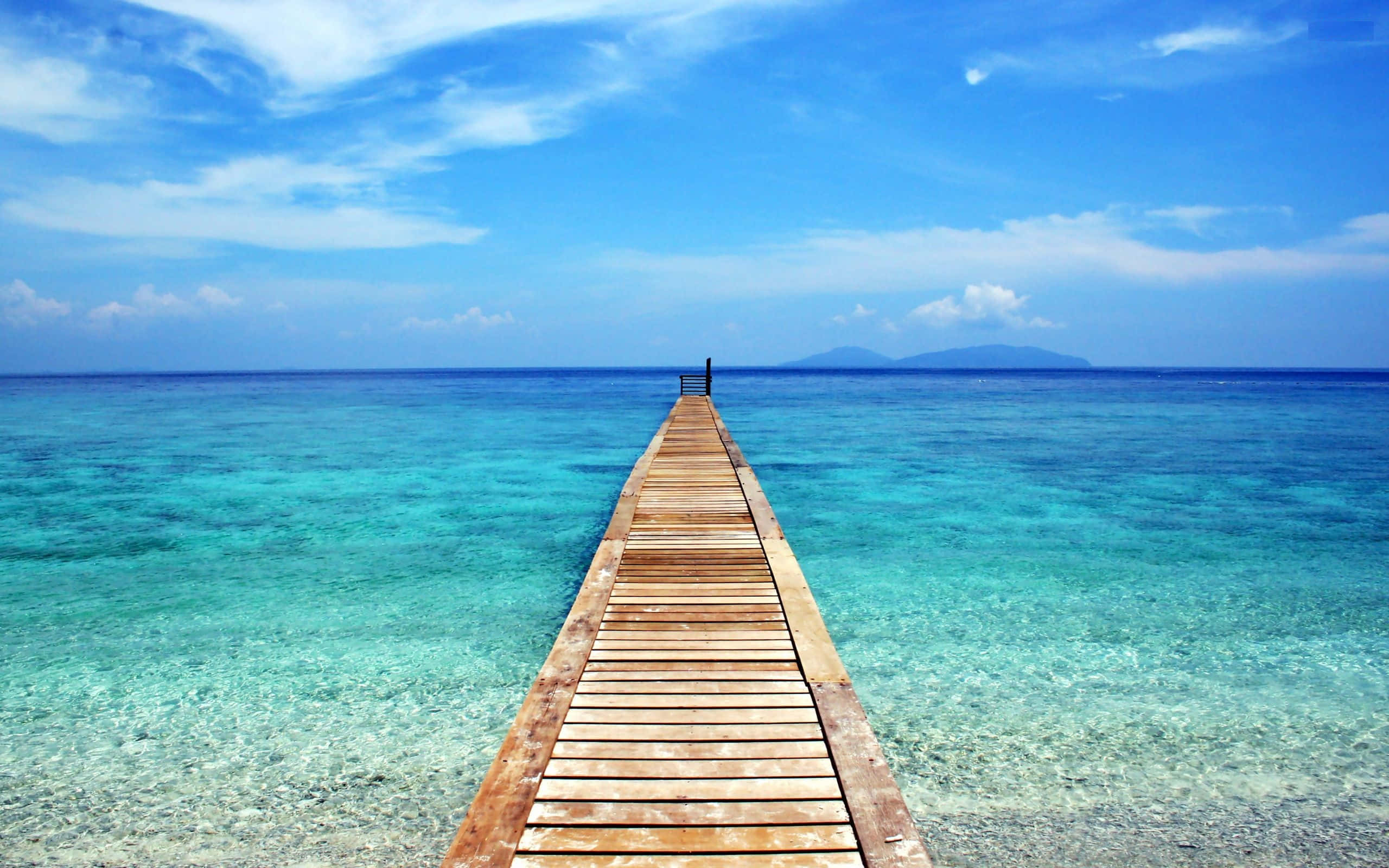 Bali Beach 桌布 壁紙 — 一條長長的木製碼頭延伸至清澈碧綠的海水中，上方是藍天白雲。