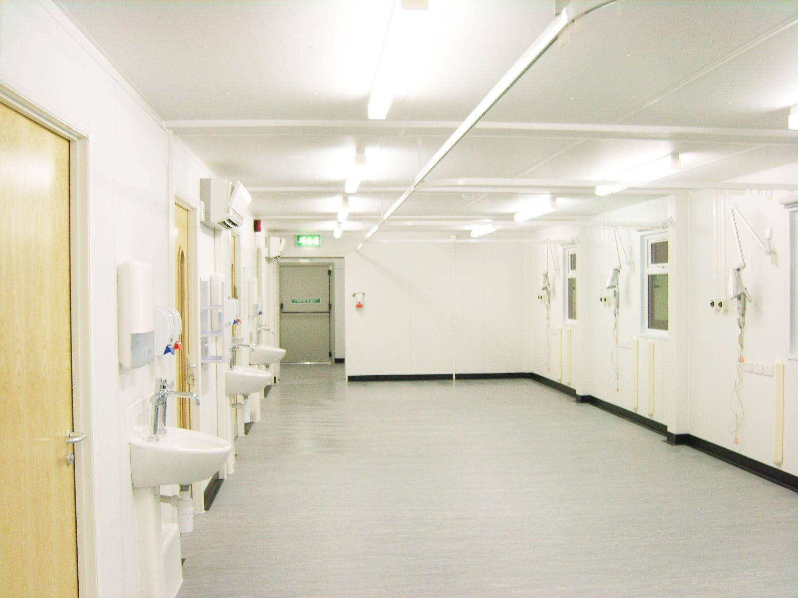 hallway 桌布 壁紙 — 一條長長的無菌醫院走廊，白色牆壁、洗手台和醫療設備在明亮的螢光燈下。