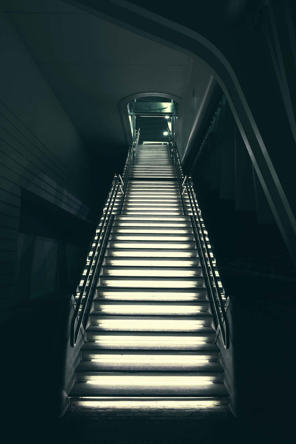 stairs 桌布 壁紙 — 一條長長的照明樓梯在隧道般的天花板下，帶著發光的台階和彎曲的欄杆，向上延伸進黑暗之中。