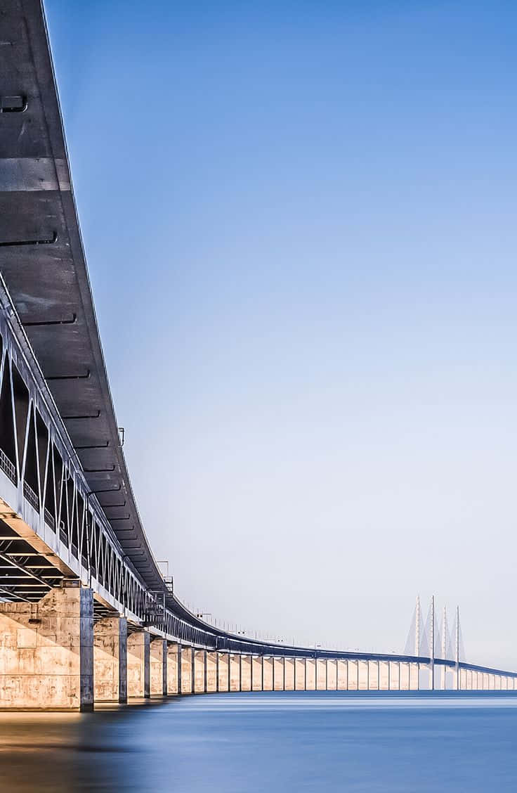 風景 桌布 壁紙 — 一條長長的現代橋樑在晴朗的藍天下優雅地彎曲在平靜的水面上。