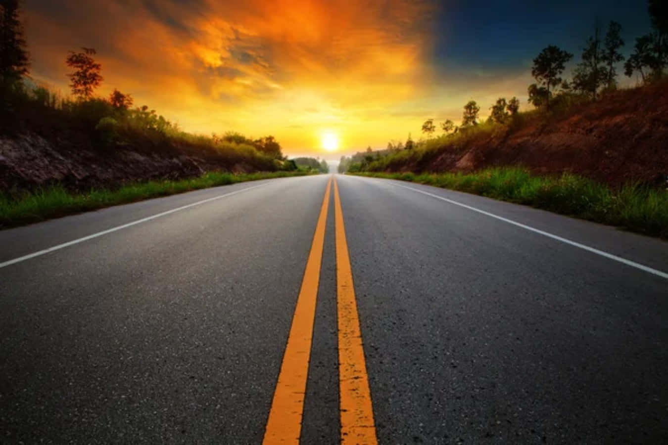 Highways 桌布 壁紙 — 一條長長的直路伸向充滿活力的日落，兩旁有橙色的雲彩和綠色的草山。