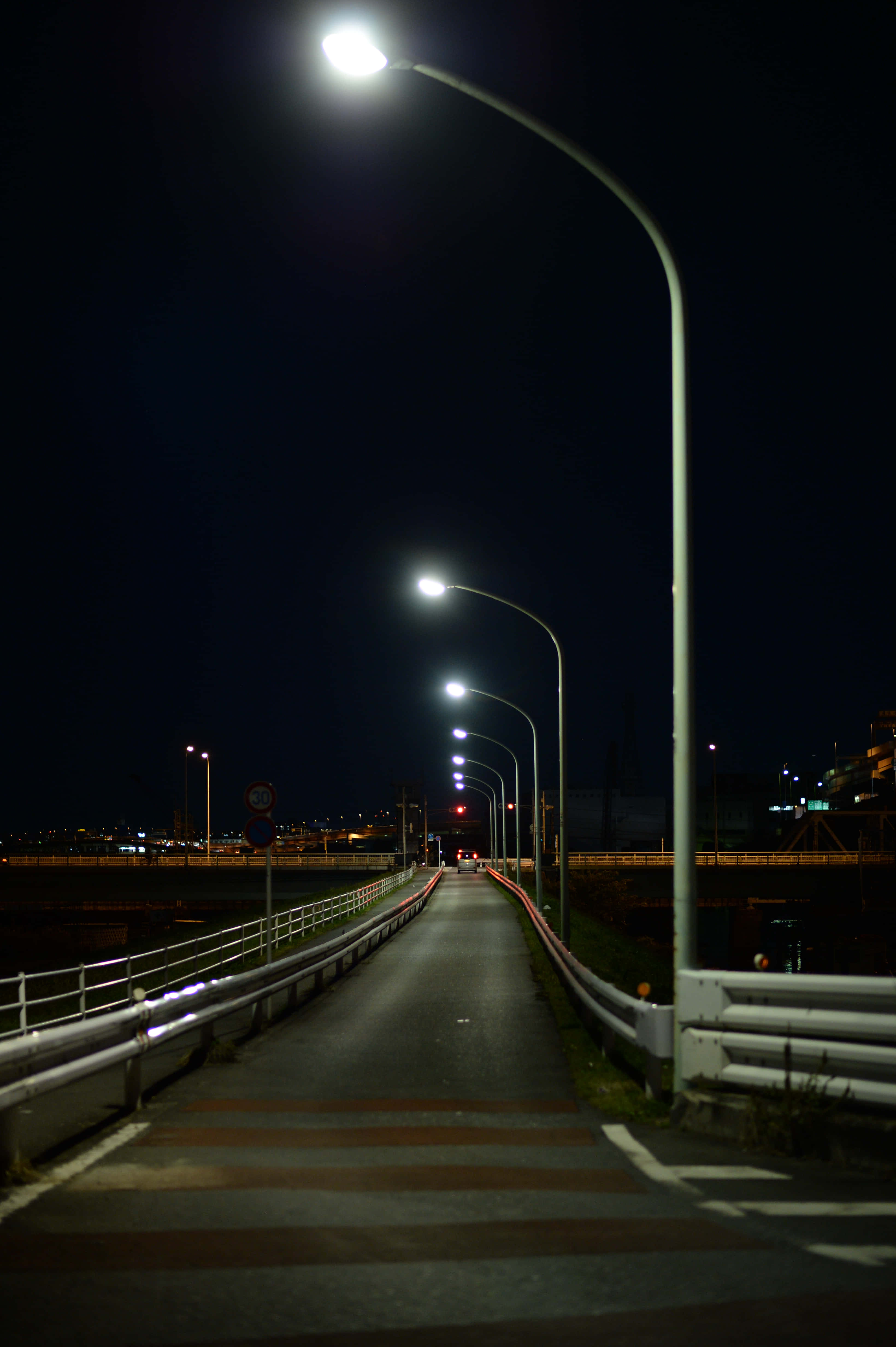 Street Light 桌布 壁紙 — 一條長長的直路在明亮的街燈下延伸至漆黑的夜晚，地平線上有遠處的城市燈光。