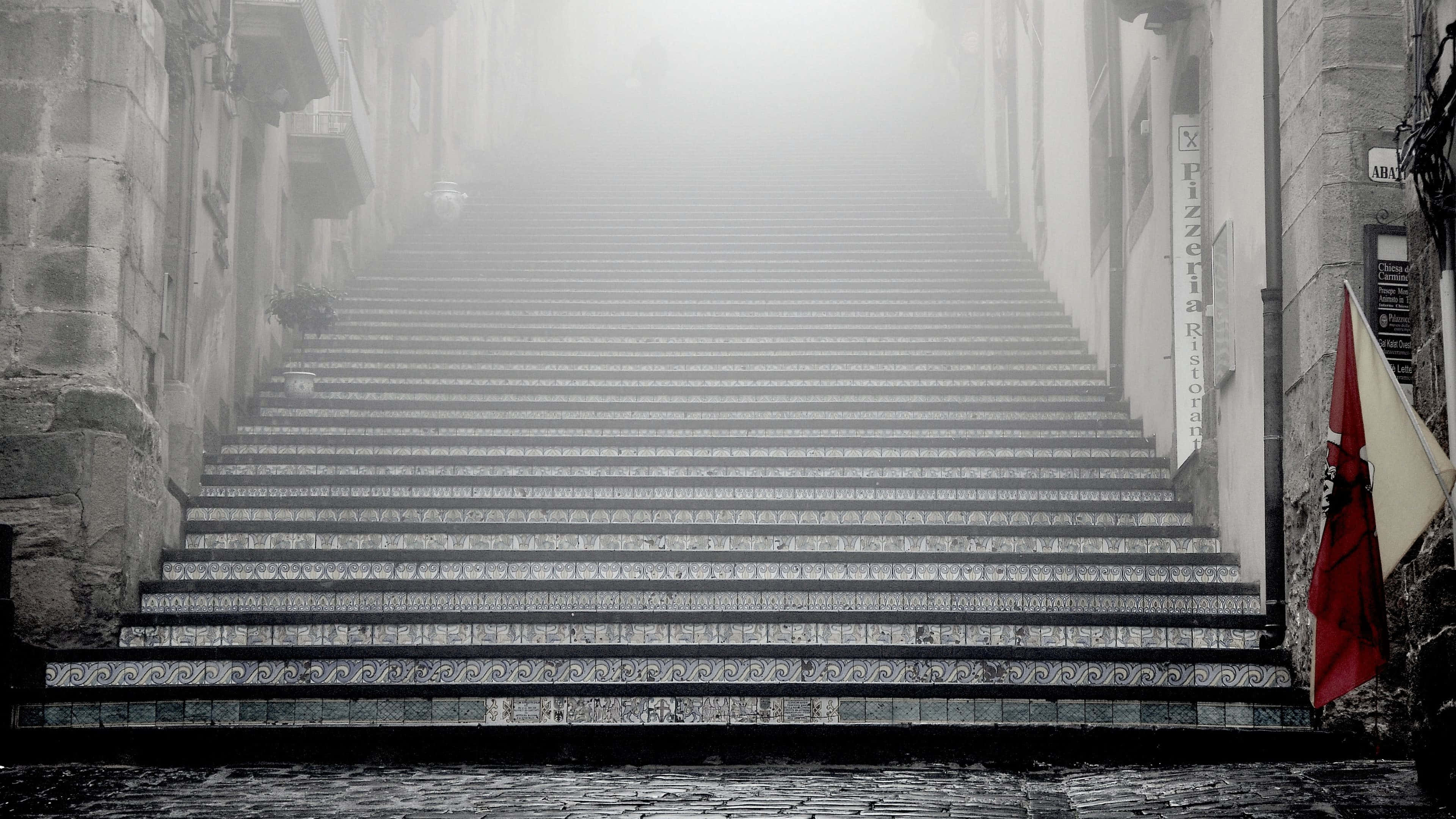 Steps 桌布 壁紙 — 一條長長的石階梯在舊建築之間延伸進濃霧中，右側掛著一面紅旗。