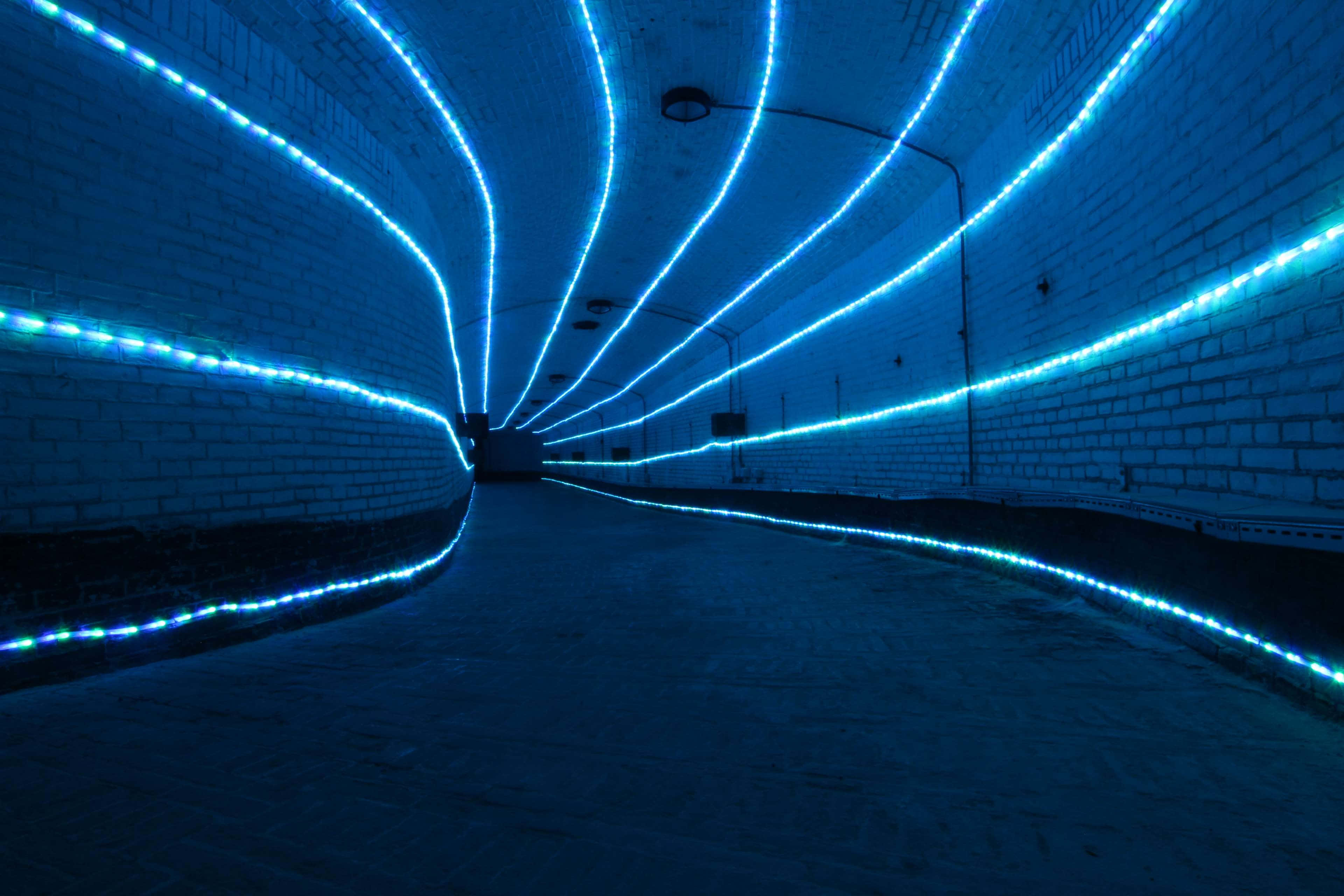 LED 桌布 壁紙 — 一條長長的磚砌隧道，由充滿活力的藍色LED燈條沿牆壁和天花板彎曲照明，營造出未來主義的發光通道。
