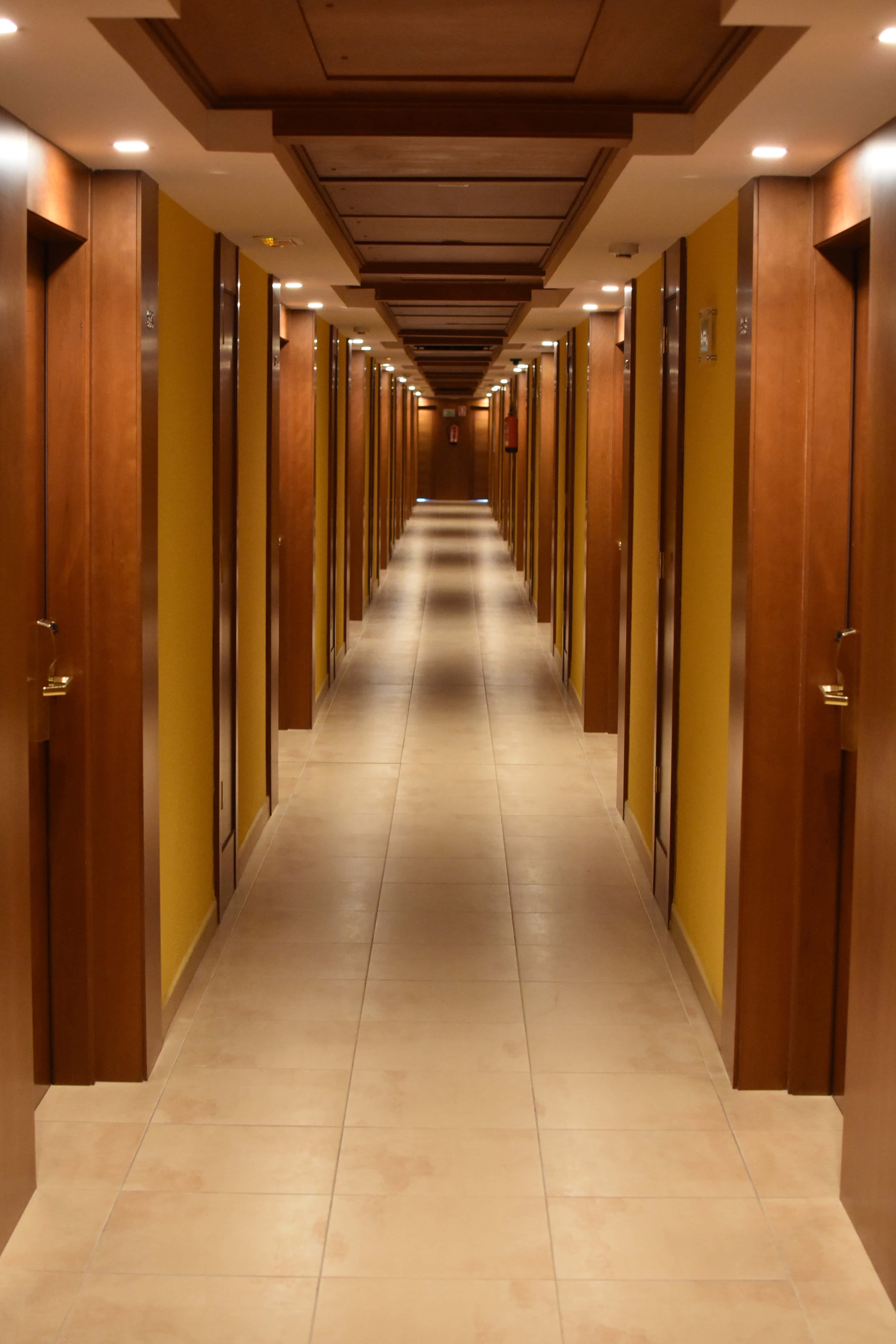 Hotel 桌布 壁紙 — 一條長長的飯店走廊，木門和黃色牆壁在溫暖的環境燈光中逐漸消失。