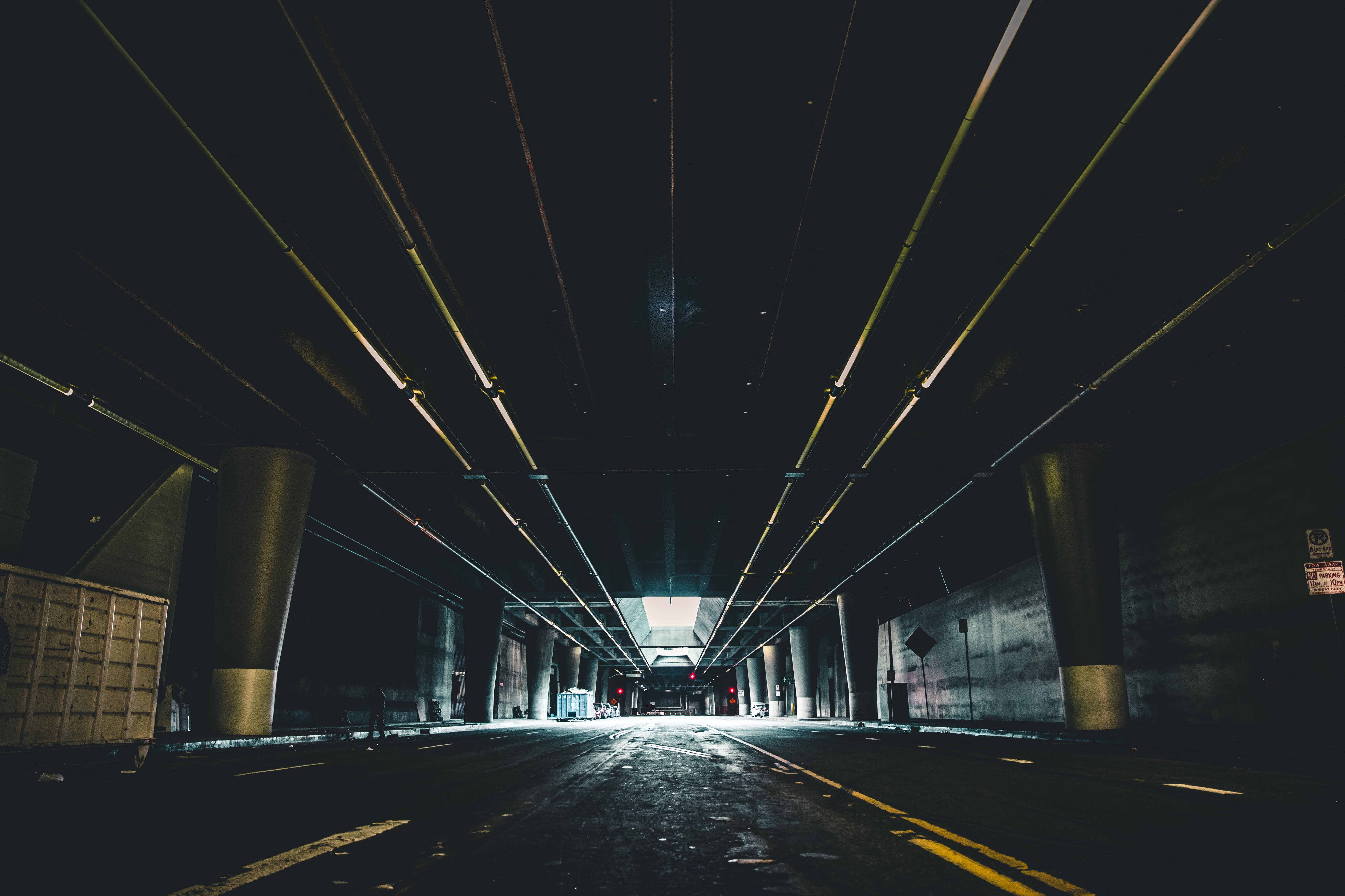 Underground 桌布 壁紙 — 一條長長的黑暗隧道，有發光的黃色燈光和混凝土柱，通往遠處明亮的出口。