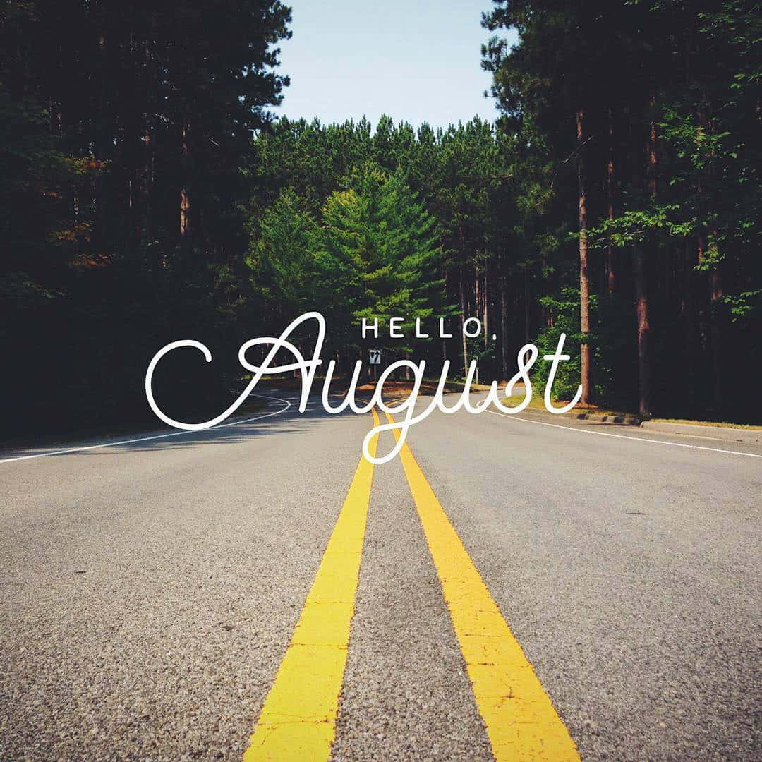 August 桌布 壁紙 — 一條陽光明媚的森林道路，帶有黃色中心線，通向高大的綠色樹木，在清澈的藍天下，白色文字寫著hello august。
