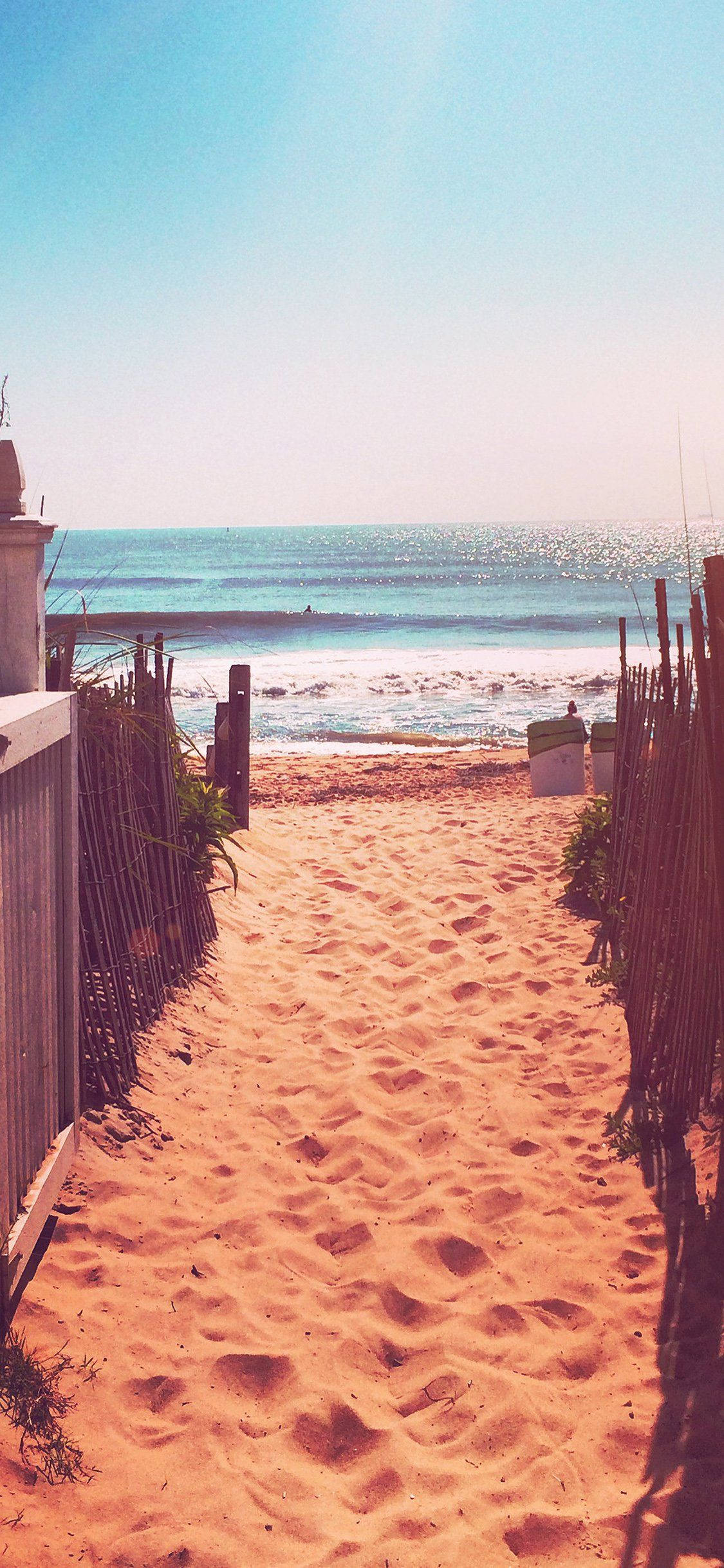 iPhone X Beach 桌布 壁紙 — 一條陽光明媚的沙質小徑，兩旁有木柵欄，通向清澈藍天下碧綠色的海洋。