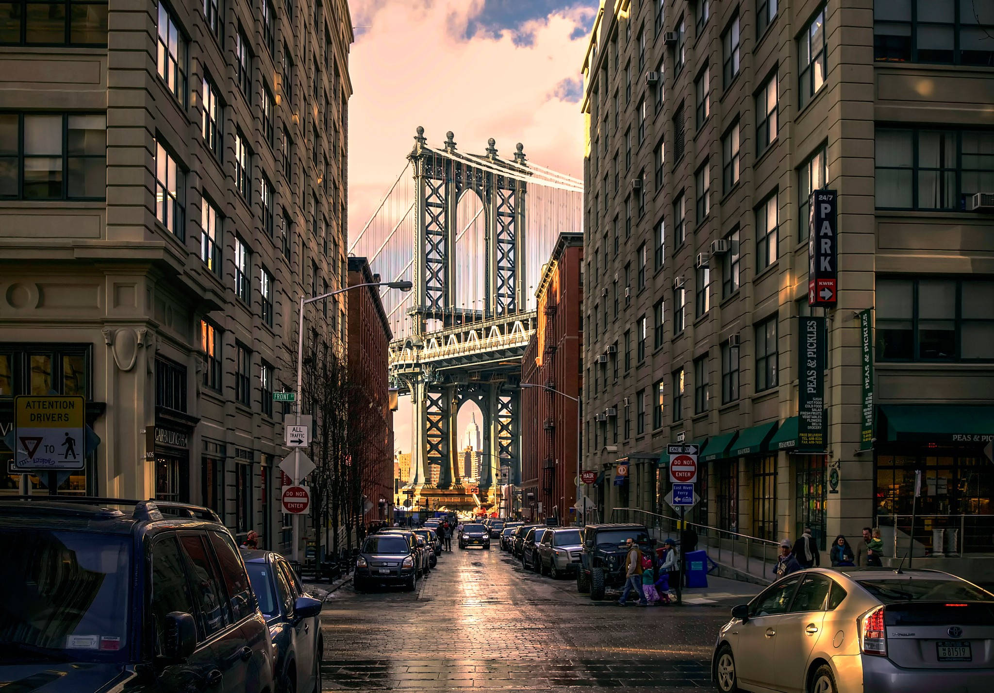 manhattan 桌布 壁紙 — 一條陽光明媚的紐約市城市街道，兩旁高樓大廈林立，遠處曼哈頓大橋高聳入雲。