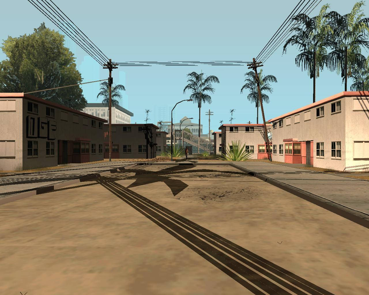 GTA 聖安地列斯 桌布 壁紙 — 一條陽光普照的城市街道，兩旁有棕櫚樹和低矮建築物，頭頂上是清澈的藍天和電線。