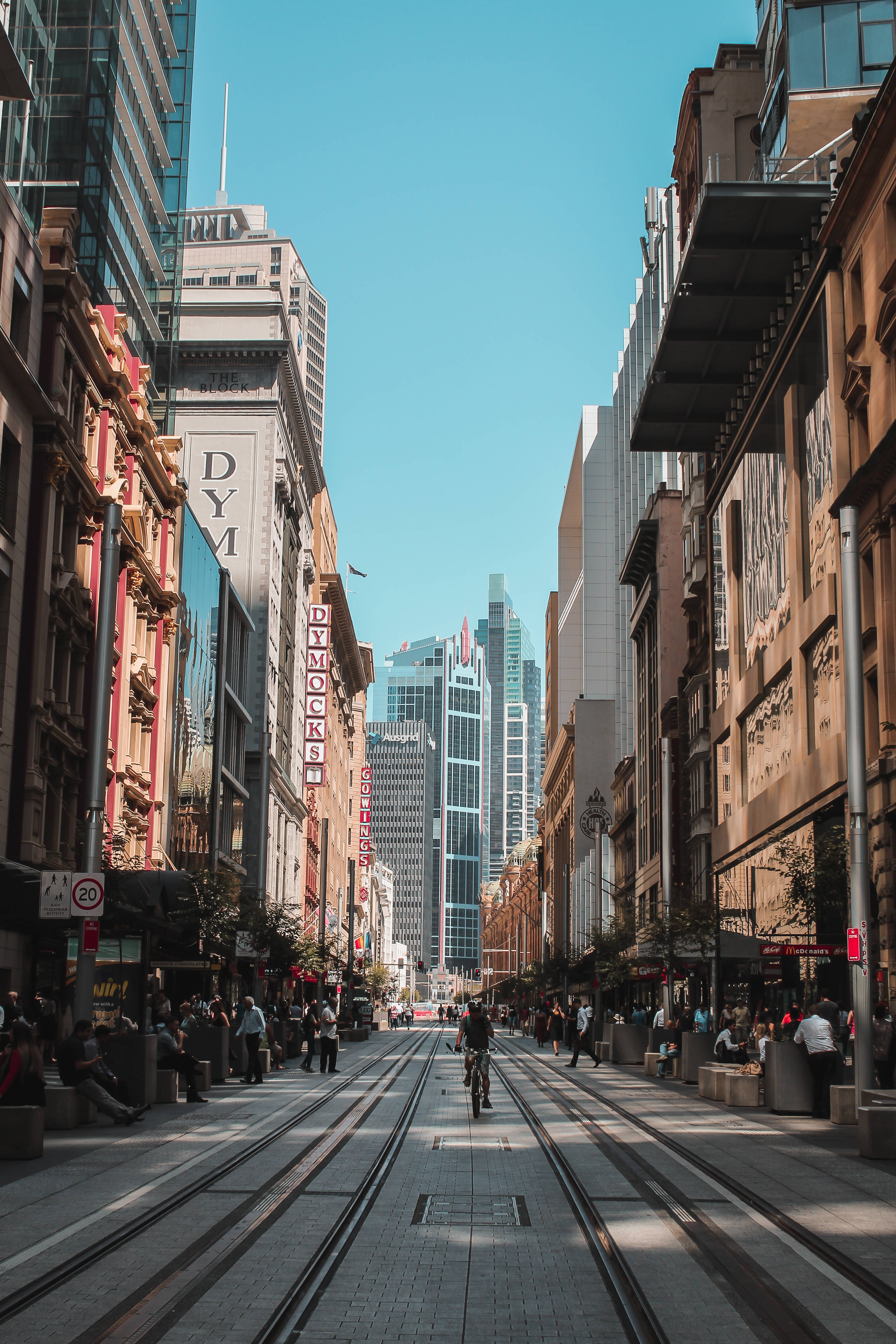 Sydney 桌布 壁紙 — 一條陽光普照的城市街道，電車軌道通向高聳的摩天大樓，天空清澈湛藍。