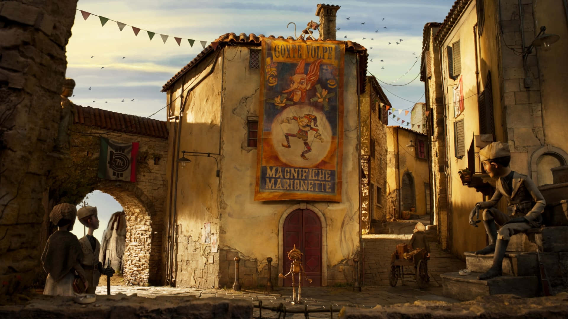 Guillermo Del Toro's Pinocchio 桌布 壁紙 — 一條陽光普照的歐洲村莊街道，有石頭建築、紙糊公仔和懸掛在風化屋頂之間的節日橫幅。