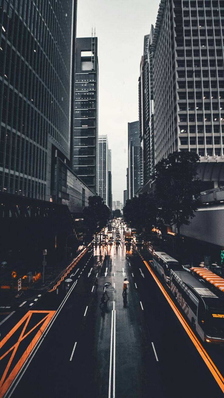 New York 桌布 壁紙 — 一條雨中的城市街道，兩旁是高聳的摩天大樓，帶有發光的橙色巴士專用道和潮濕反光的路面。
