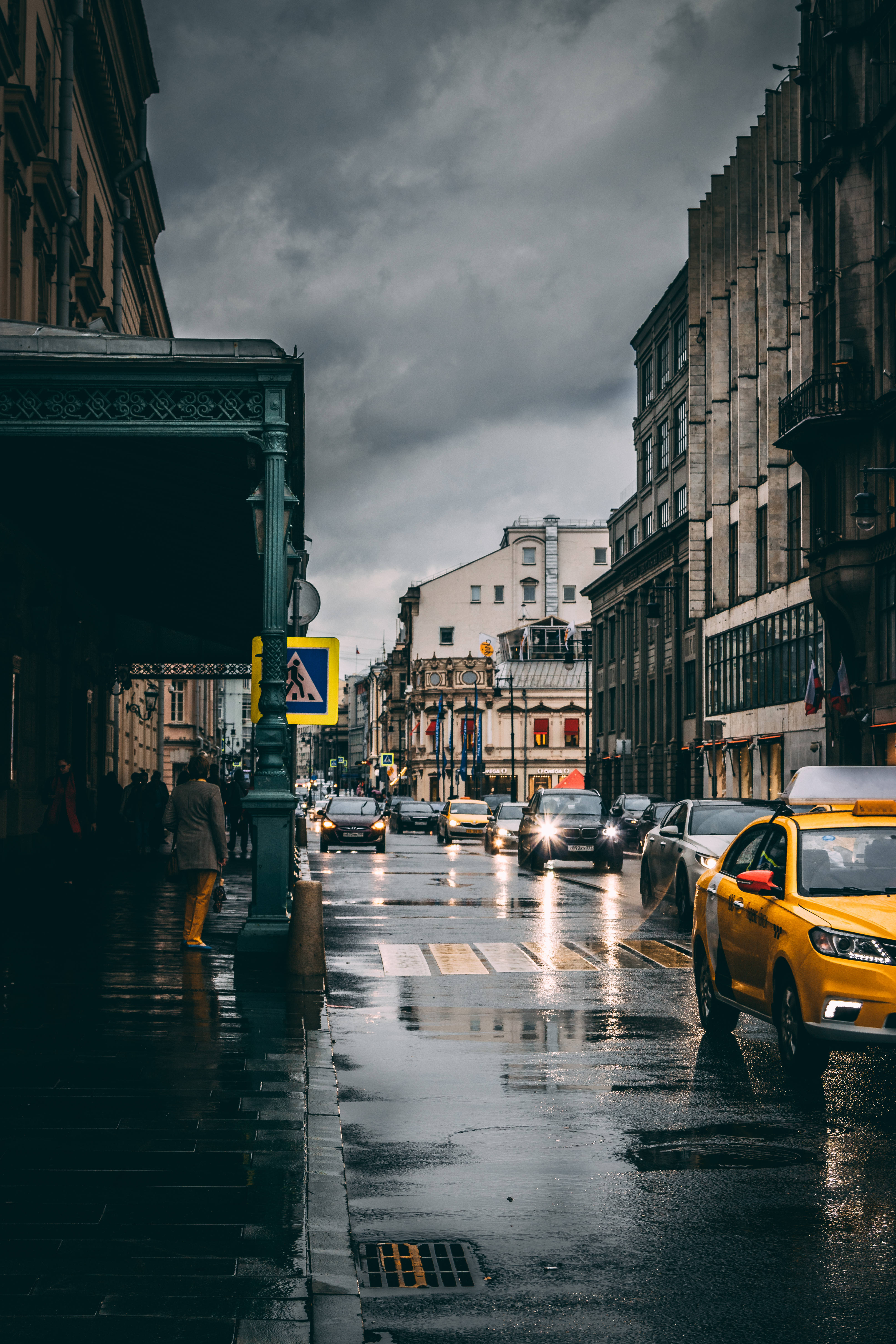 mood 桌布 壁紙 — 一條雨中的城市街道，濕漉漉的路面反射著車頭燈，天空陰沉。