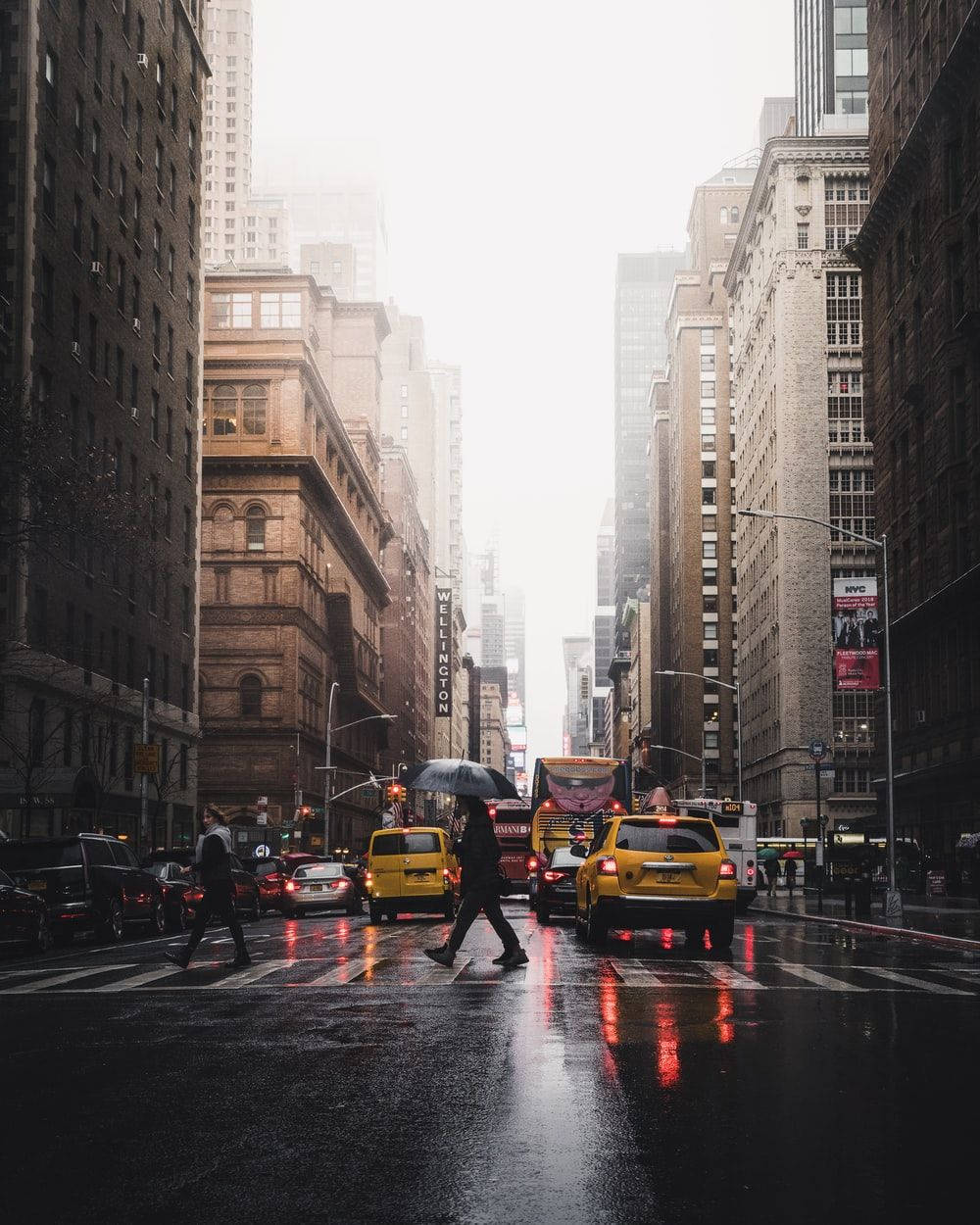 New York 桌布 壁紙 — 一條雨中的城市街道，行人撐著雨傘過馬路，黃色的士在濕漉漉的路面上反射紅燈。