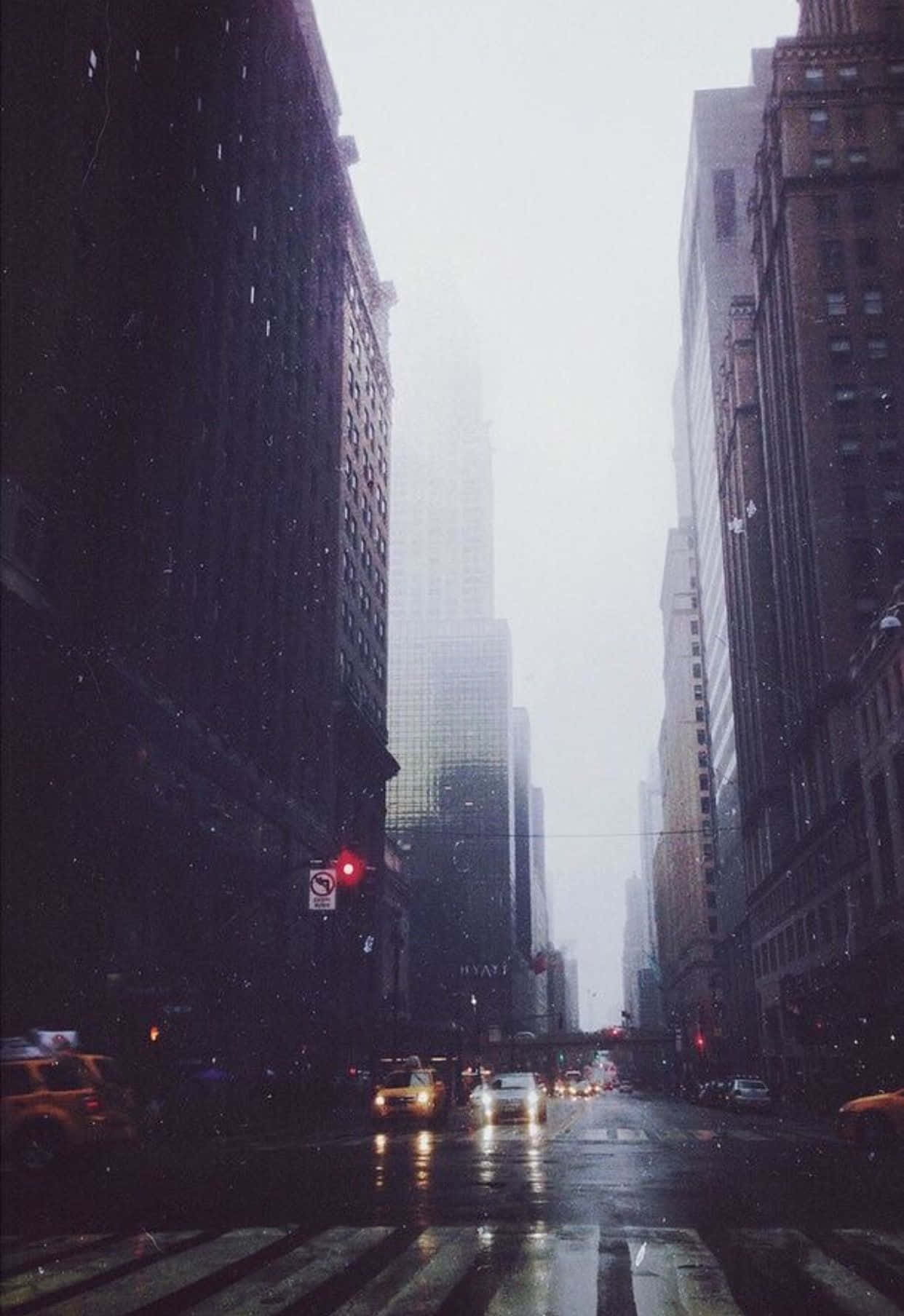 Foggy Aesthetic 桌布 壁紙 — 一條雨中的城市街道，高樓大廈、濕漉漉的路面，以及穿過薄霧的閃爍車頭燈。