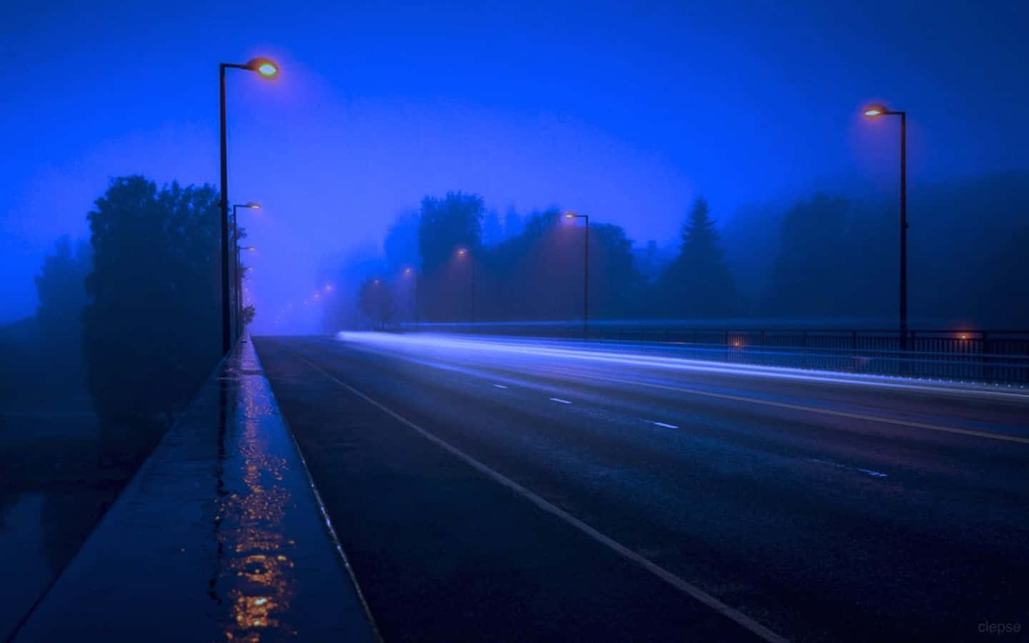 桌布 壁紙 — 一條霧氣瀰漫的夜晚道路，被發光的街燈照亮，汽車燈光的條紋逐漸消失在霧中。