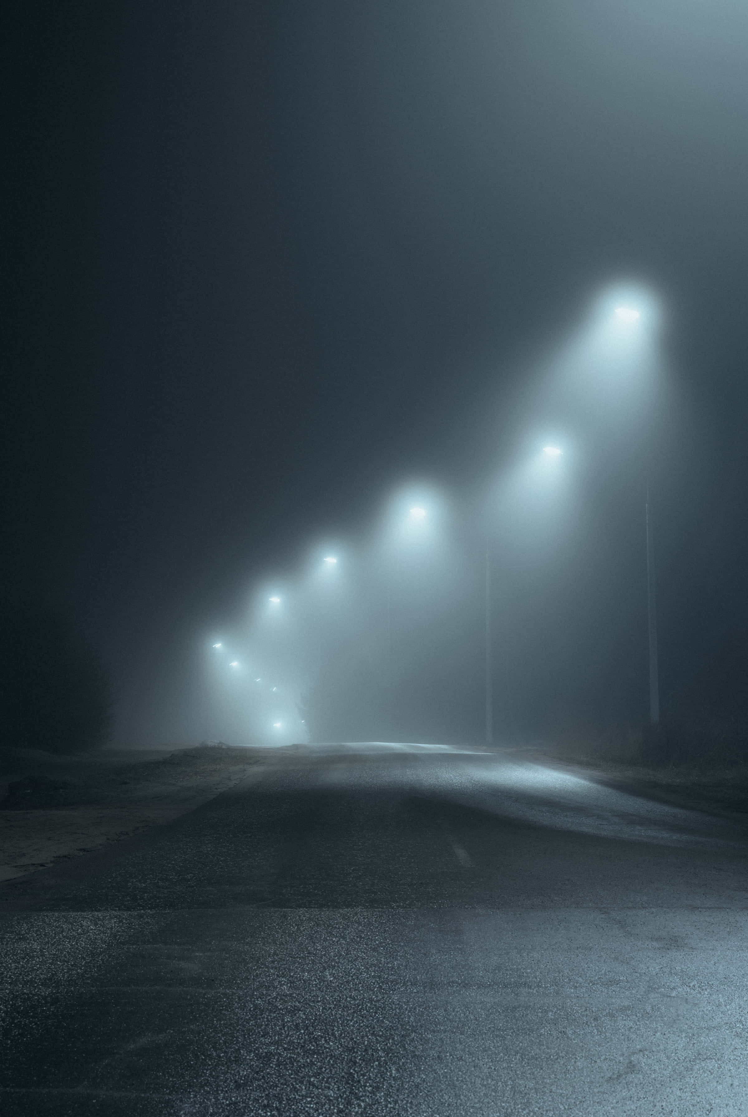 Dark Road 桌布 壁紙 — 一條霧氣瀰漫的夜路，由一排街燈照亮，在濃霧中投射出空靈的光束。
