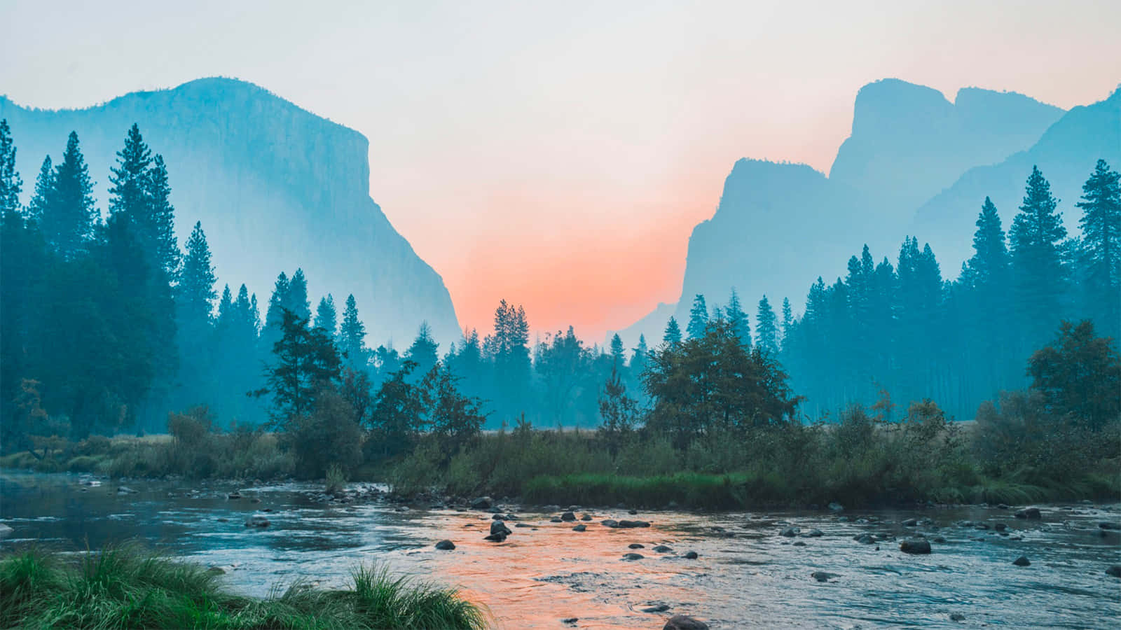 environment 桌布 壁紙 — 一條霧氣瀰漫的河流在日出時流經森林覆蓋的山谷，高聳的山脈沐浴在柔和的粉紅色和藍色光中。