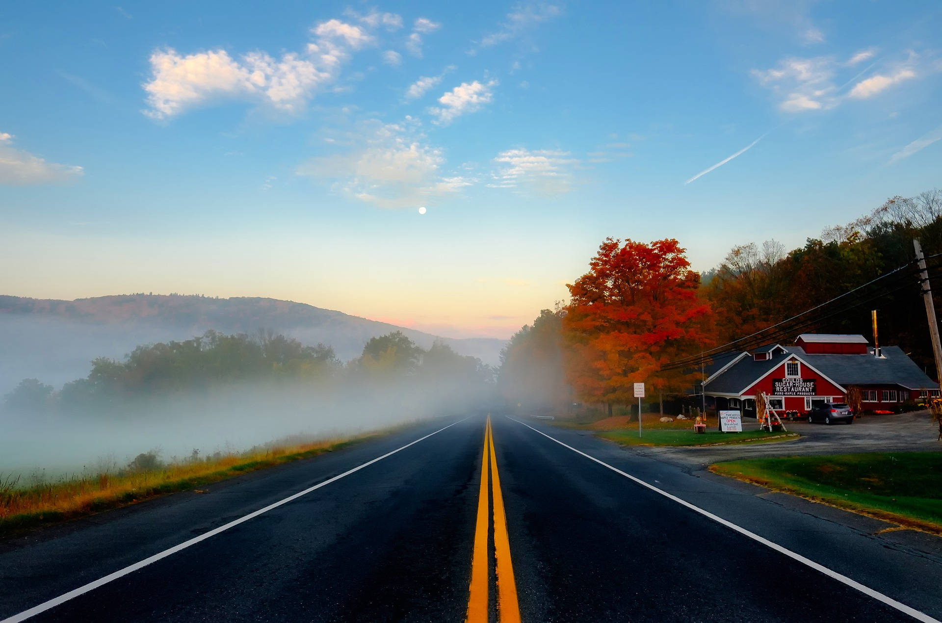 Massachusetts 桌布 壁紙 — 一條霧氣瀰漫的秋季道路，在可見月亮的柔和日出天空下，延伸向遠方的山丘。