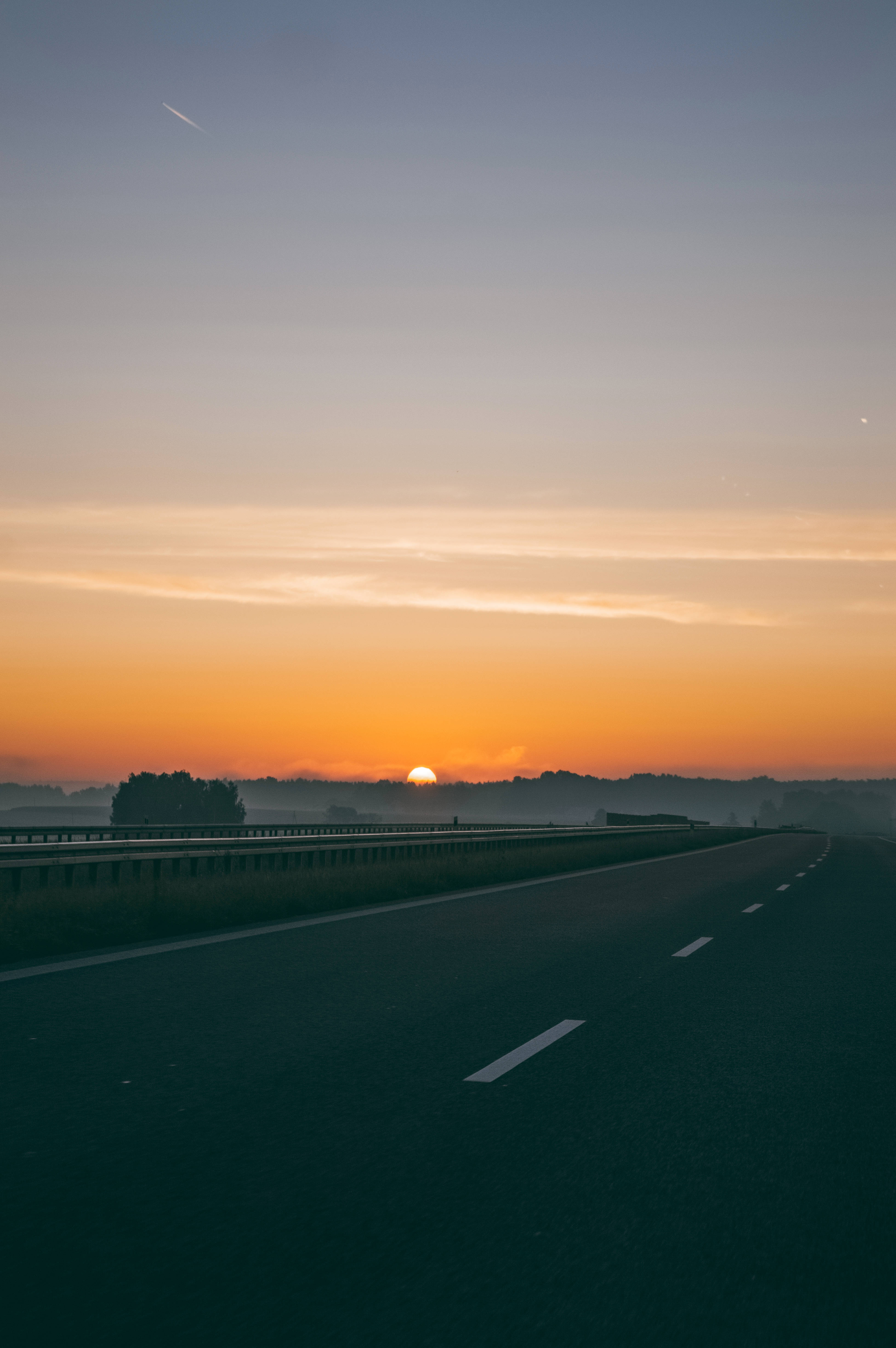Road 桌布 壁紙 — 一條霧氣瀰漫的高速公路伸向一個閃耀的日出，將天空染成溫暖的橙色和柔和的藍色調。