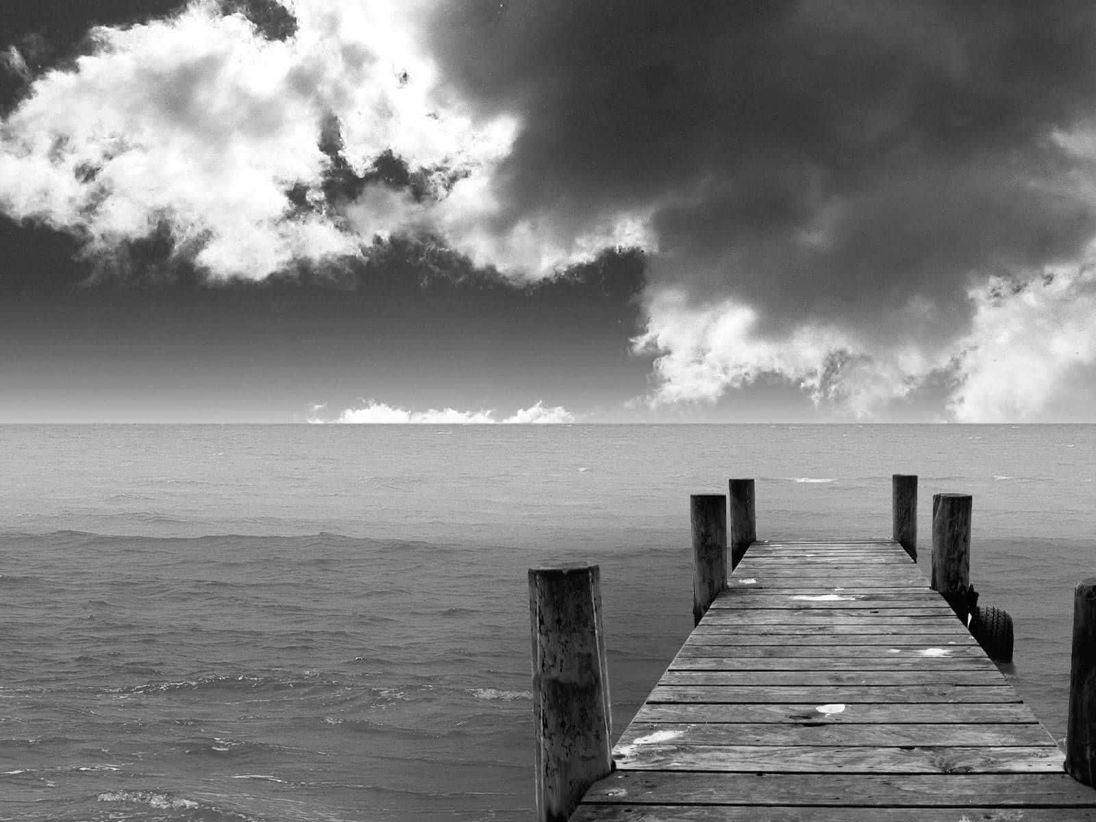 Black And White Landscape 桌布 壁紙 — 一條風化的木碼頭延伸至平靜的海面，上方是帶有漩渦狀雲層的戲劇性單色天空。