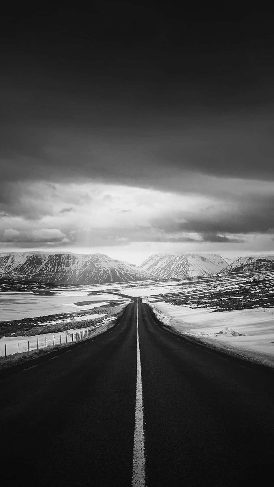 highway 桌布 壁紙 — 一條鮮明的黑白道路延伸至積雪覆蓋的山脈，天空烏雲密佈。