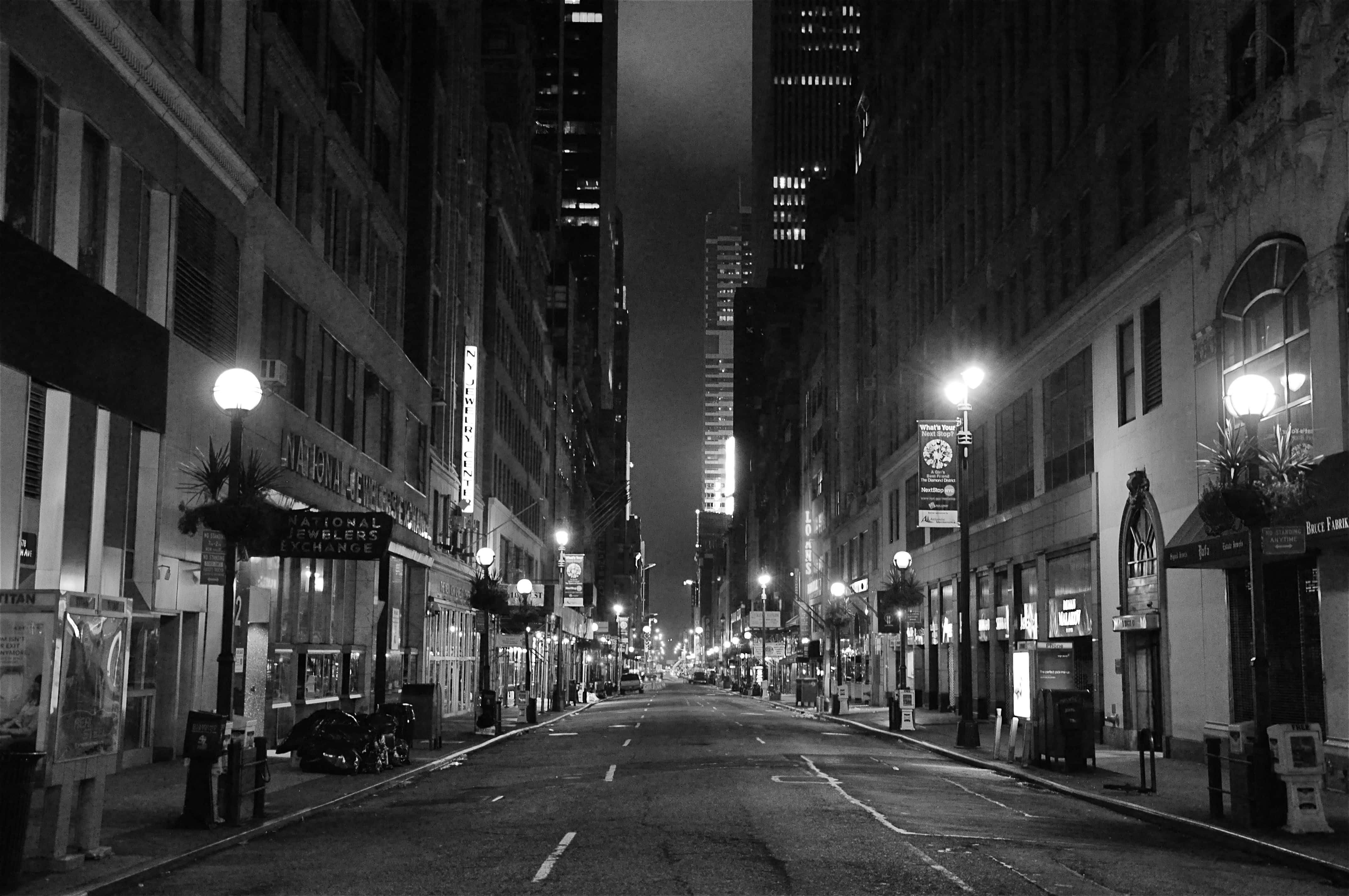 Black And White Street 桌布 壁紙 — 一條鮮明黑白對比的夜間城市街道，兩旁是高樓大廈，閃爍的燈光和停泊的汽車。