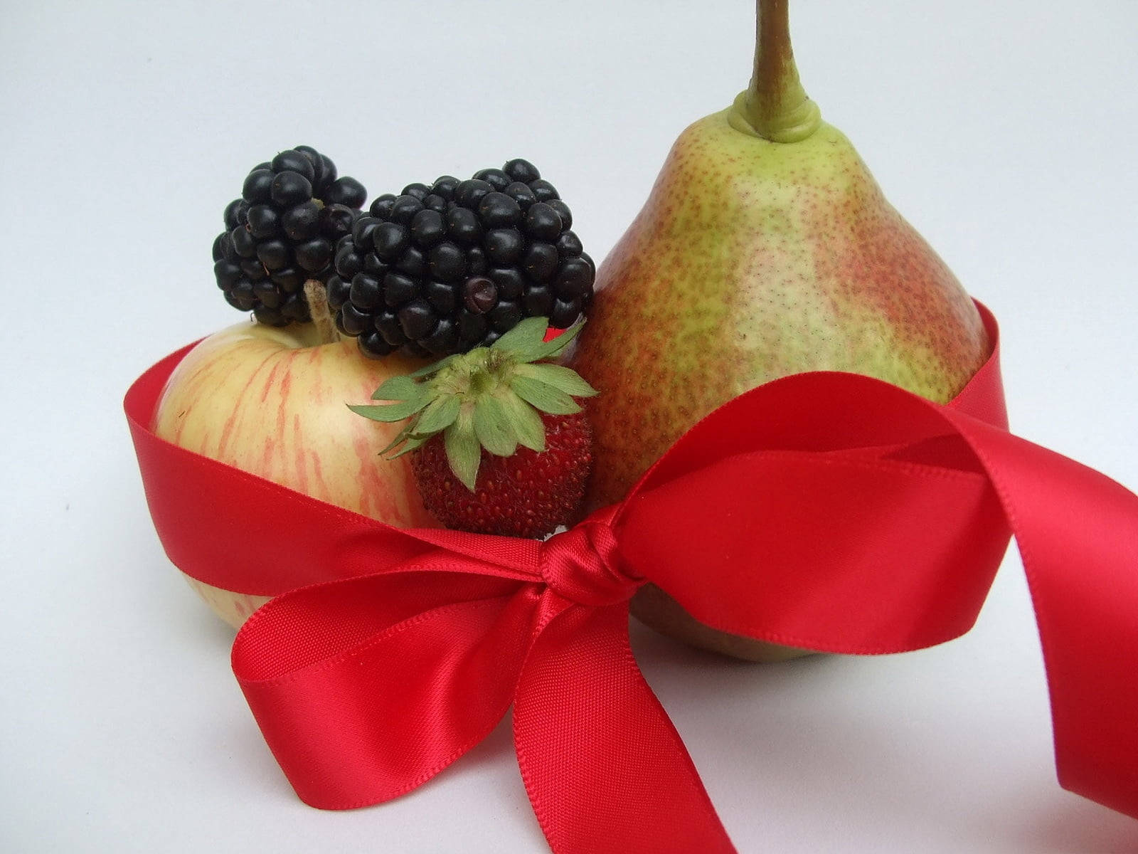 Berry 桌布 壁紙 — 一條鮮豔的紅色緞帶優雅地纏繞著梨、蘋果、草莓和黑莓，背景是潔淨的白色。