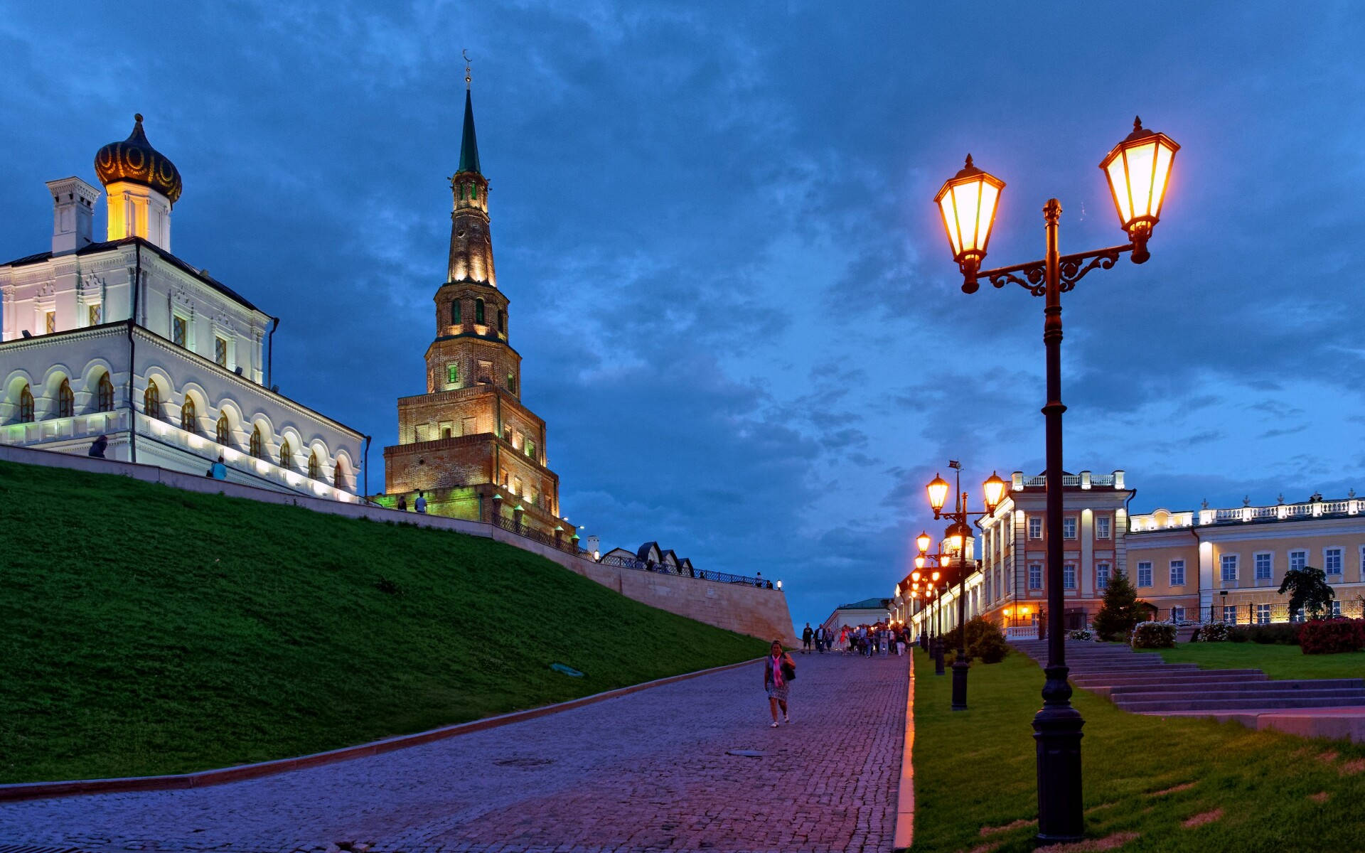 Kazan 桌布 壁紙 — 一條鵝卵石小徑蜿蜒穿過燈火通明的歷史塔樓和路燈，在深藍色的暮色天空下。