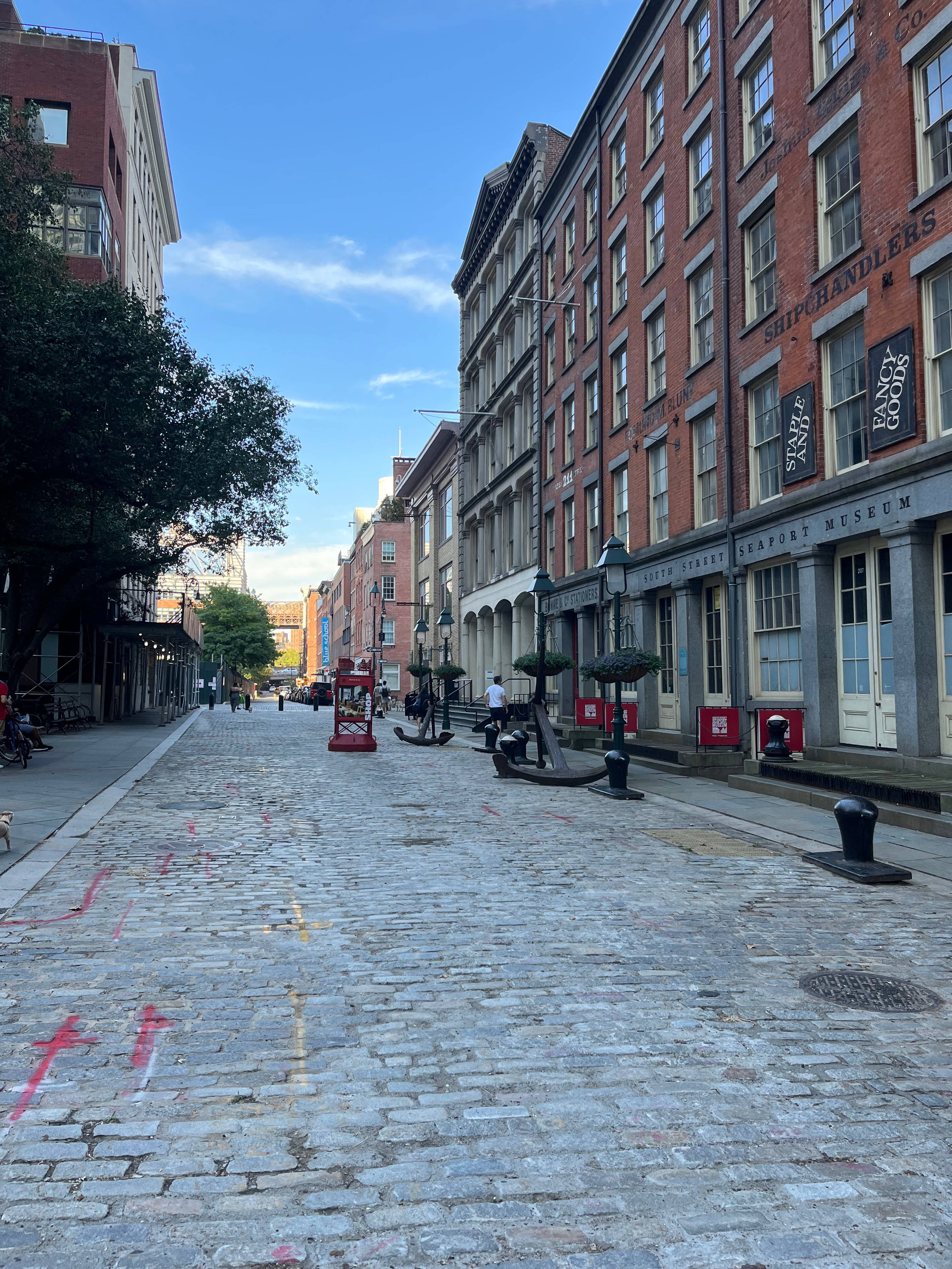 New York 桌布 壁紙 — 一條鵝卵石街道，兩旁是歷史悠久的磚造建築，天空湛藍清澈，白雲點點。