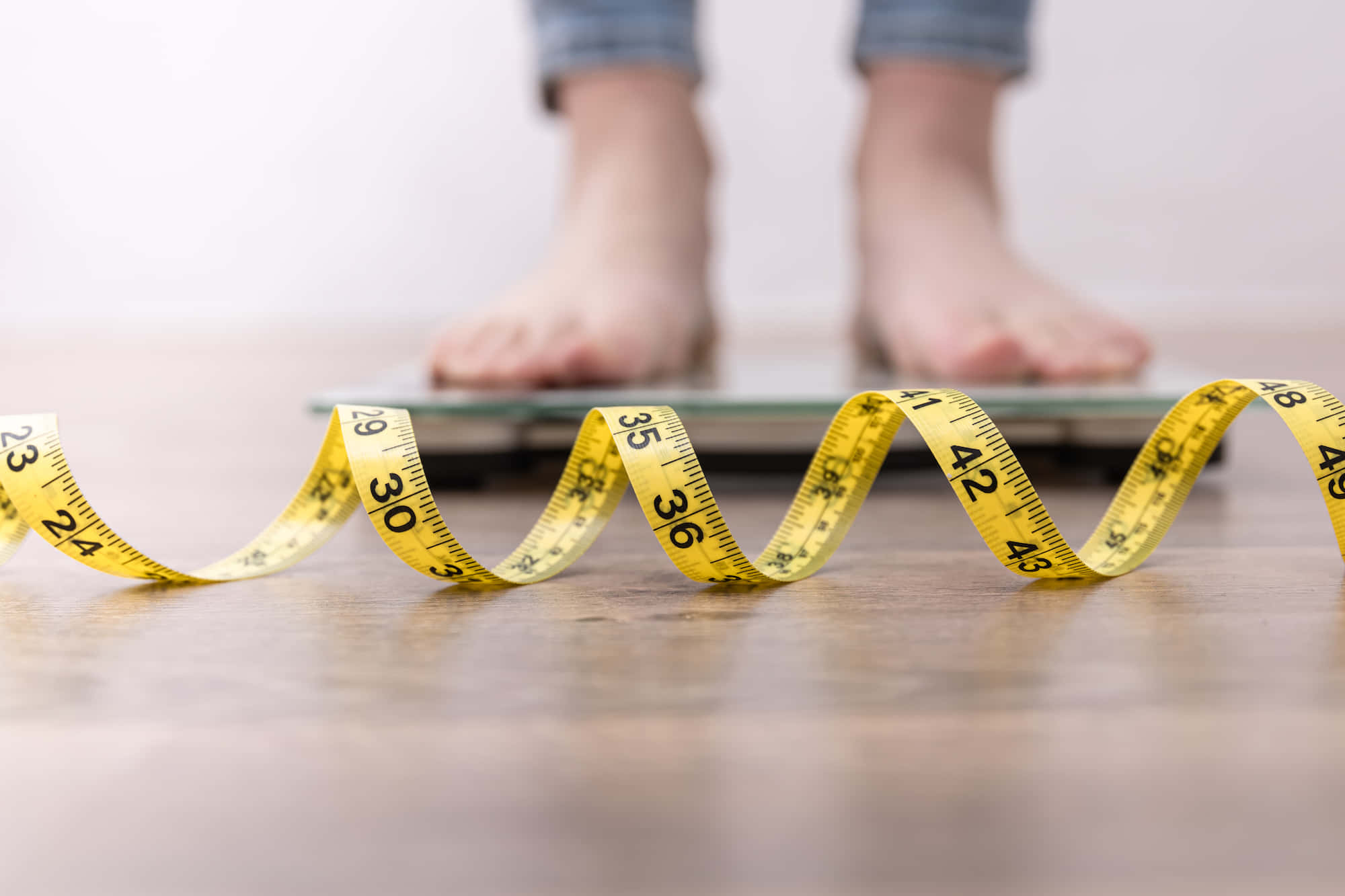 Weight Loss 桌布 壁紙 — 一條黃色軟尺在木地板上盤繞，前面有一雙赤腳站在電子秤上。