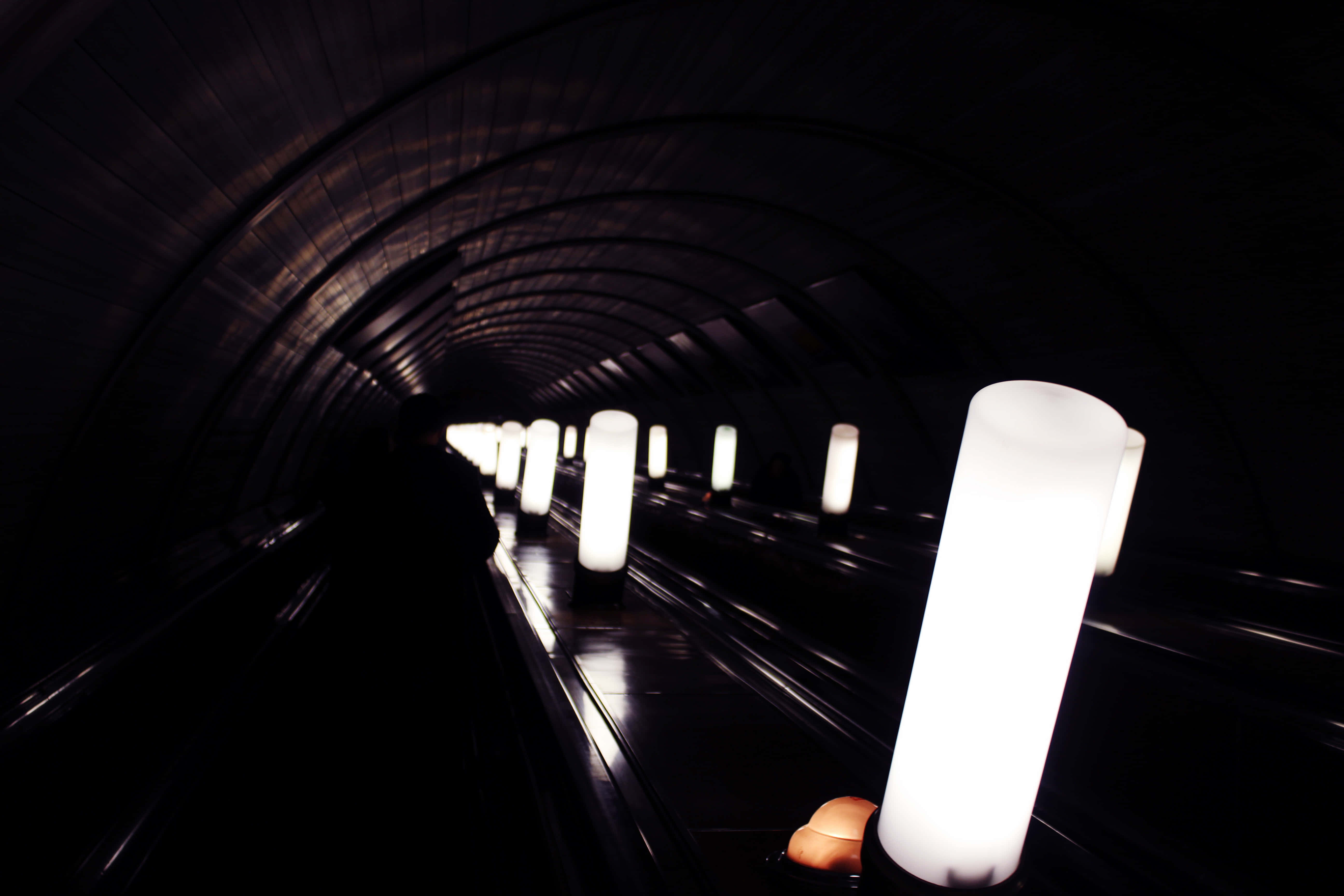 Dark Underground 桌布 壁紙 — 一條黑暗彎曲的地鐵隧道，由發光的圓柱形燈光照亮，逐漸消失在遠方。